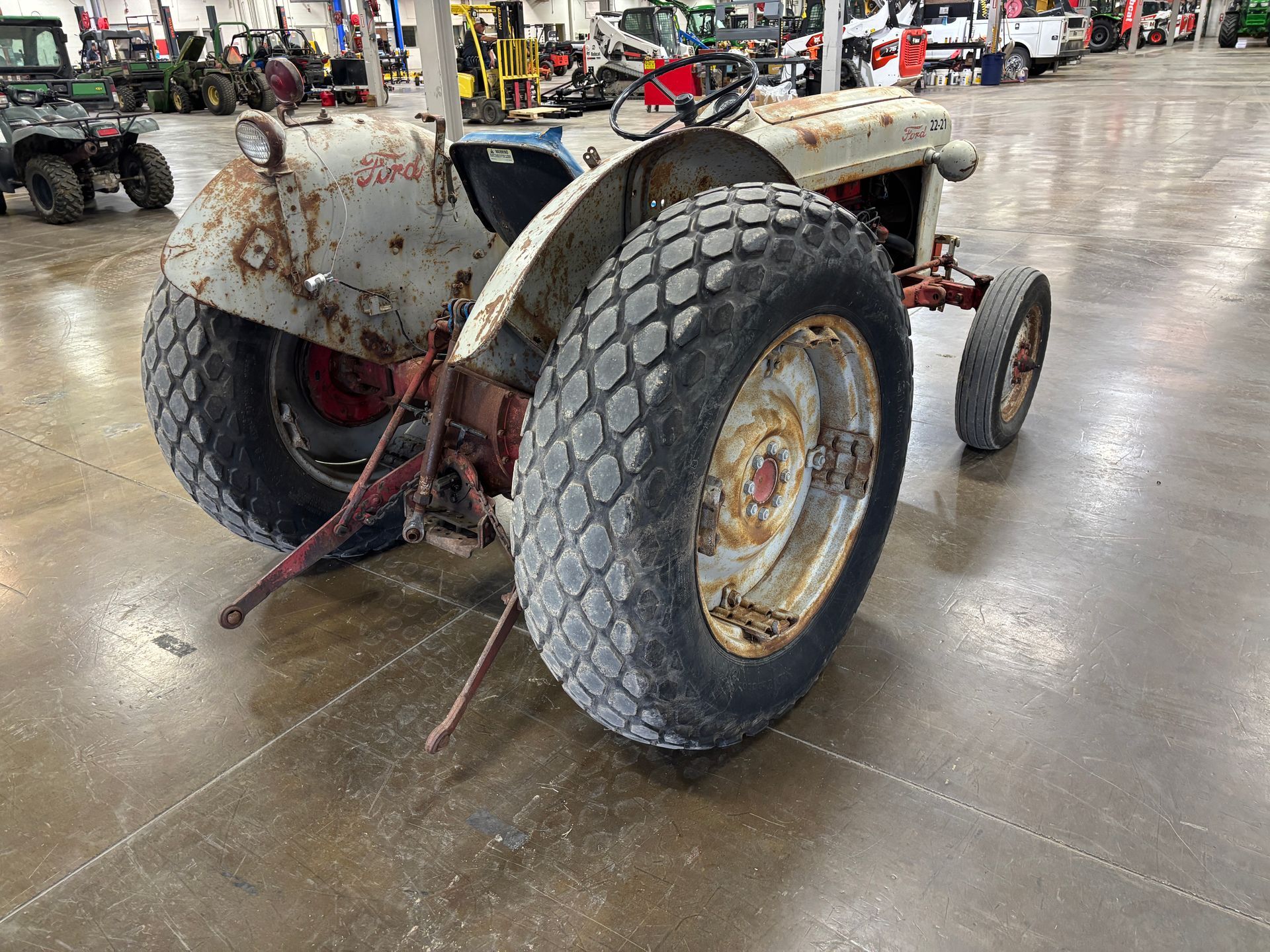 Old, weathered white tractor with large rear tires, parked indoors.