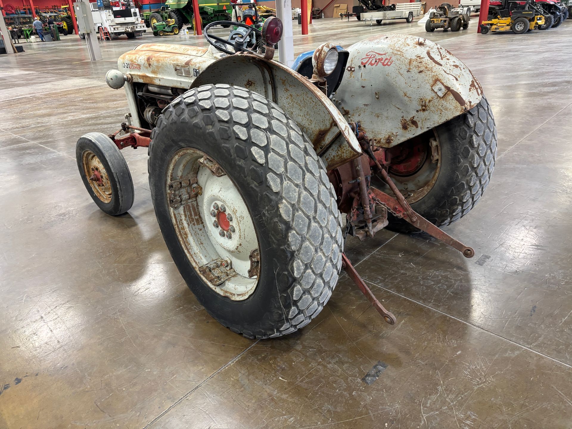 Old, weathered Ford tractor with large rear tires, parked indoors.