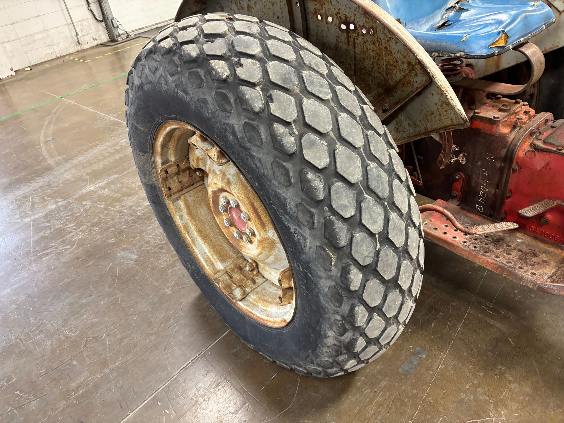 Tractor front tire with a diamond tread pattern, on a rusty wheel, indoors.