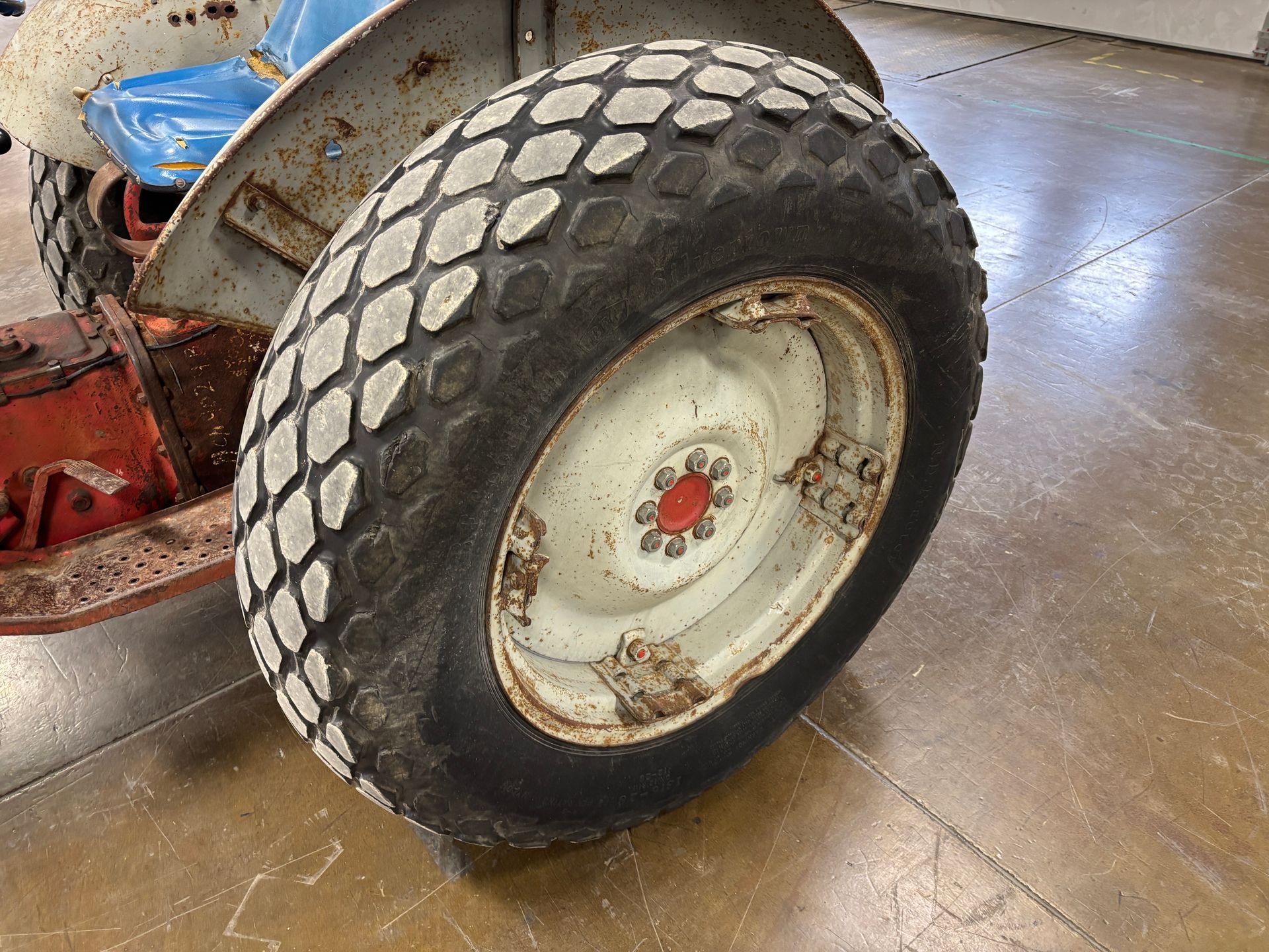 A close-up of a tractor's rear tire and wheel, with a red hub cap. The tractor is blue and orange.