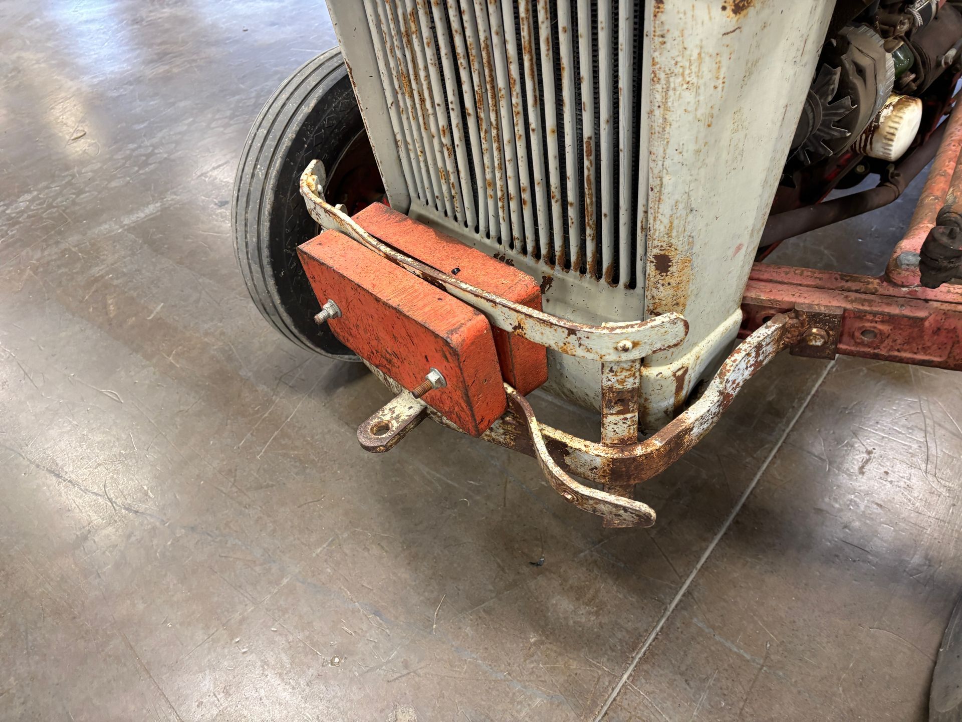 Close-up of a weathered, gray tractor's front end with a rusty grill and orange blocks attached.