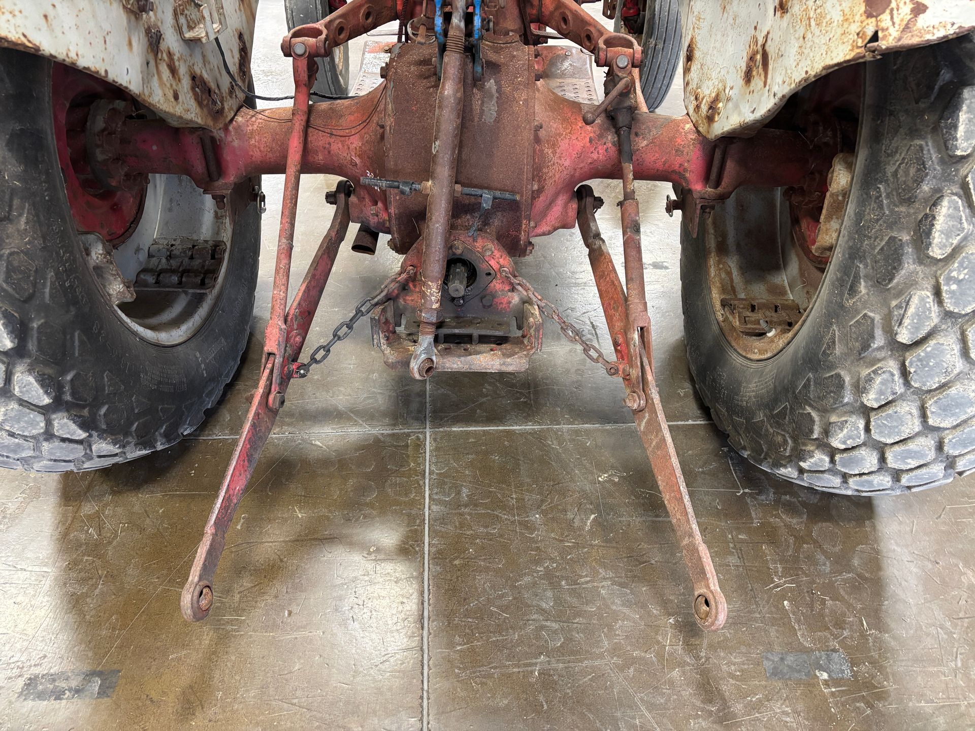 Rear view of a red and white tractor with worn tires and metal arms, set on a gray surface.