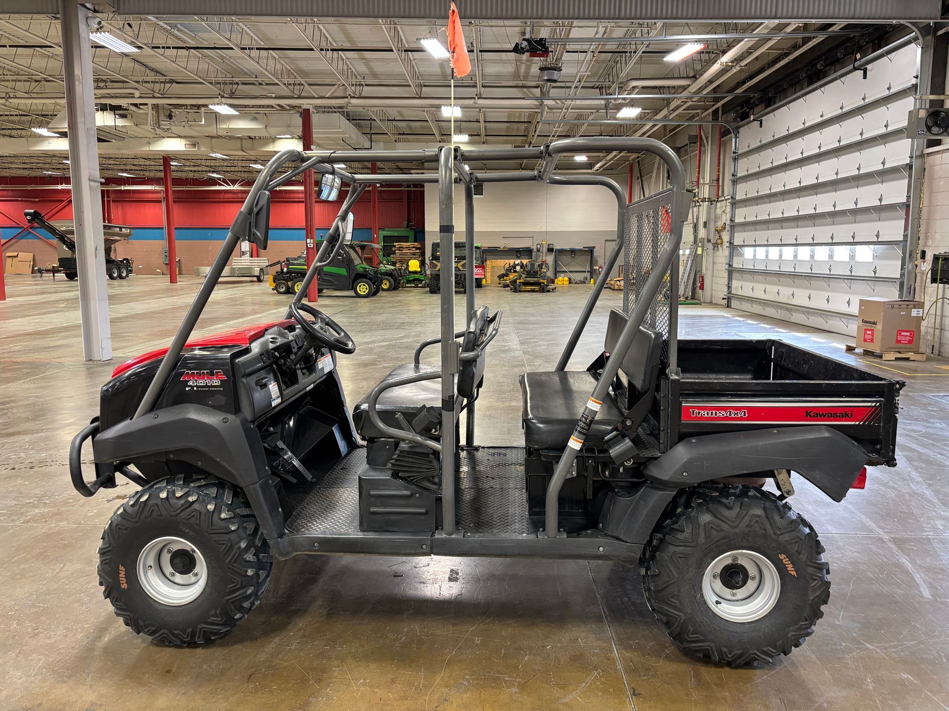 Black and red utility vehicle with roll cage and cargo bed, parked in a warehouse.