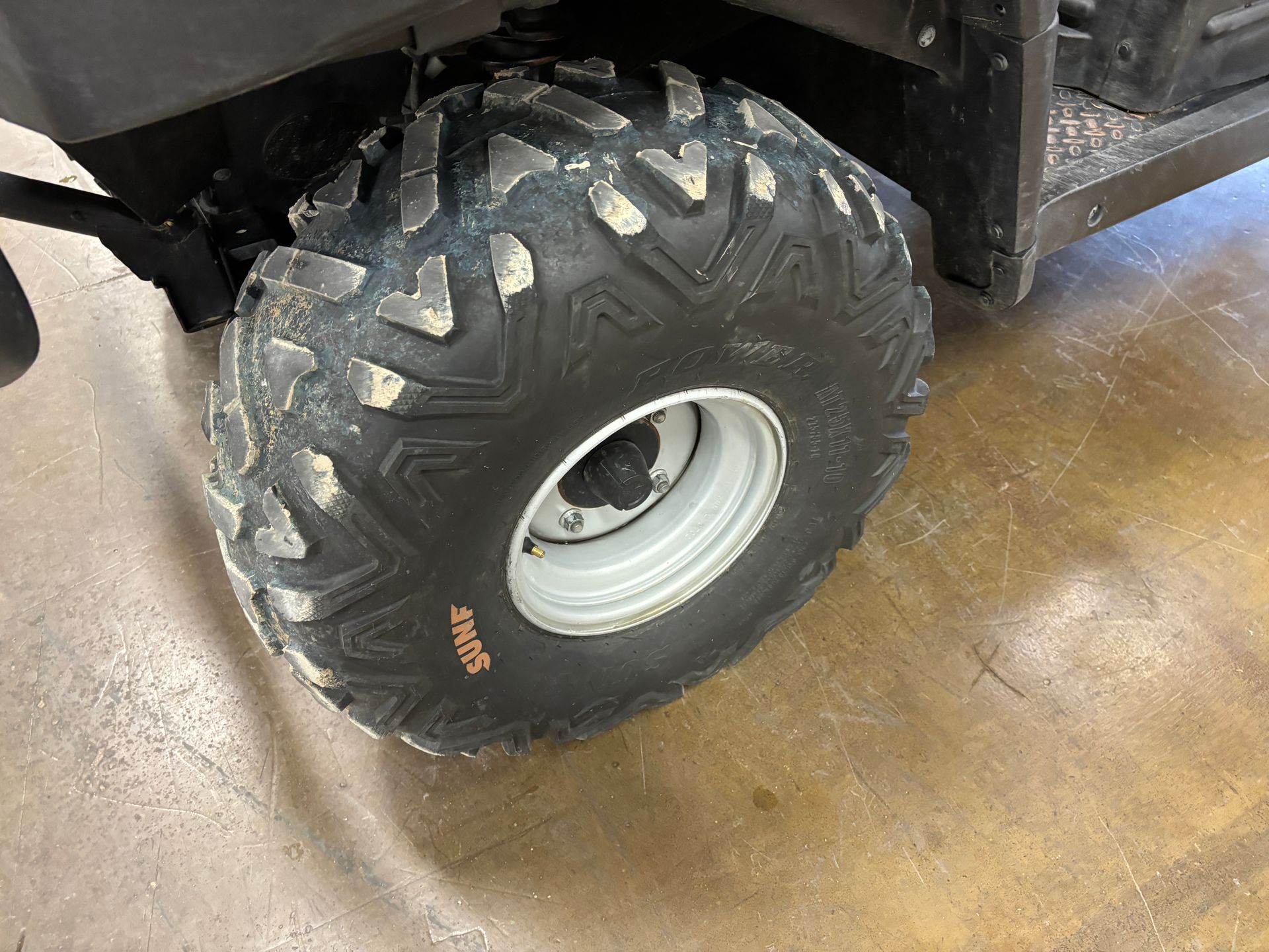 Black off-road tire on a white rim, attached to a utility vehicle. The tire is dirty.