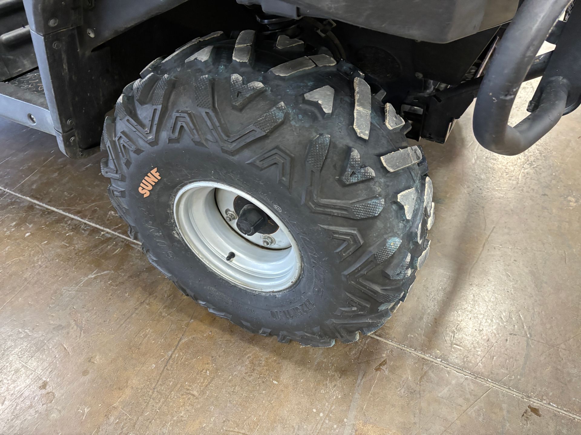 Close-up of an ATV wheel with a black tire and gray rim on a concrete floor.