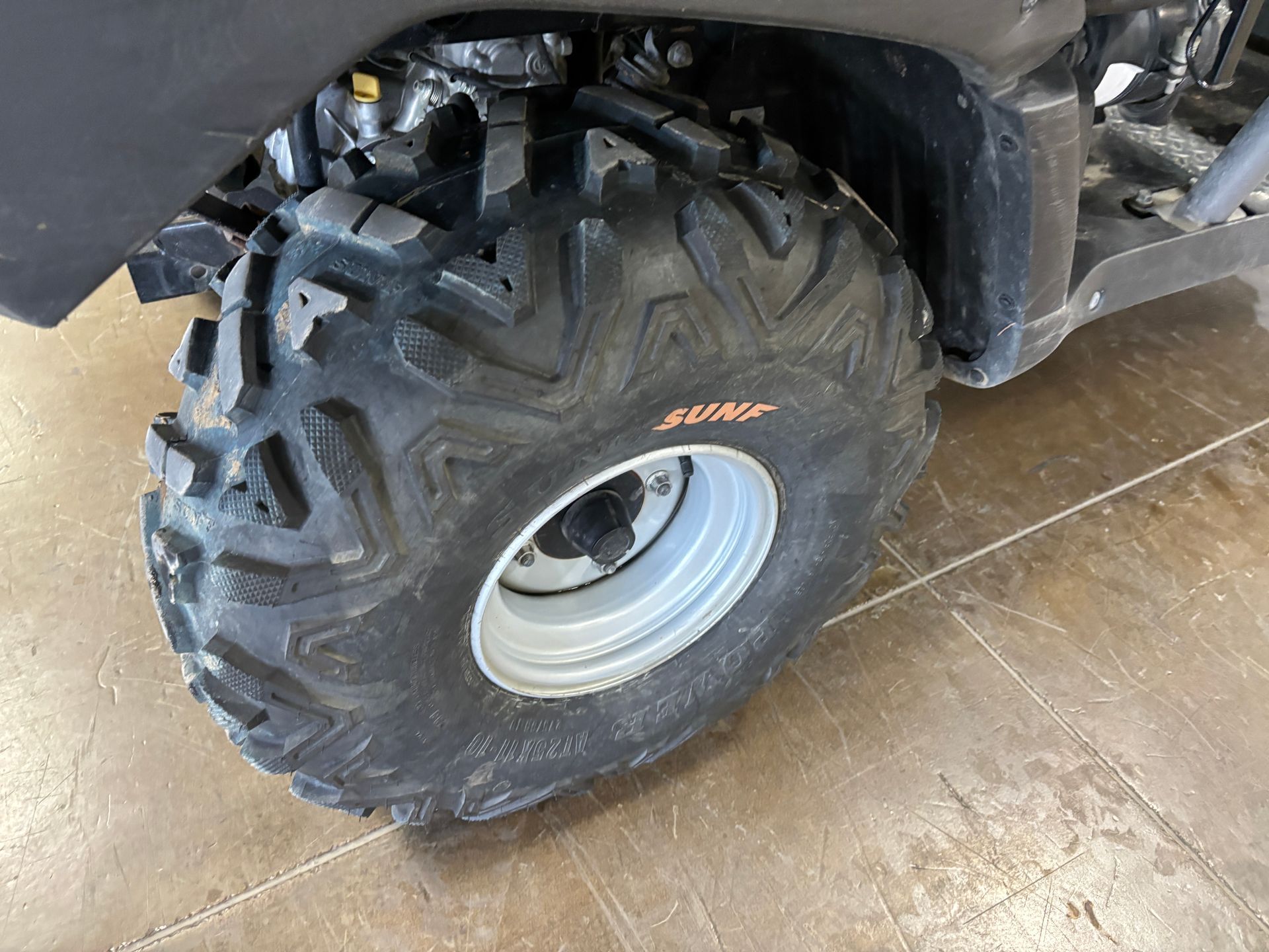 Close-up of an ATV wheel with black tire and silver rim on a concrete surface.