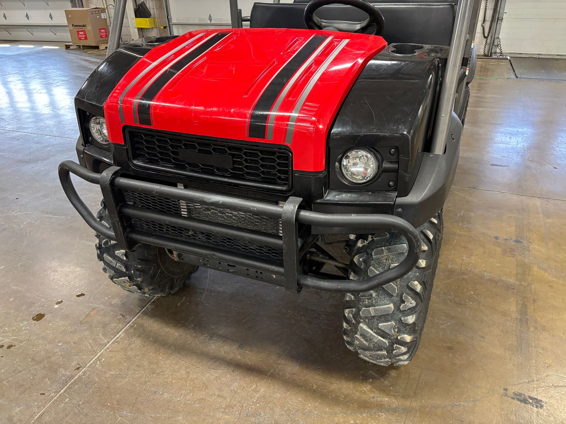 Black and red utility vehicle with brush guard, on a concrete floor.