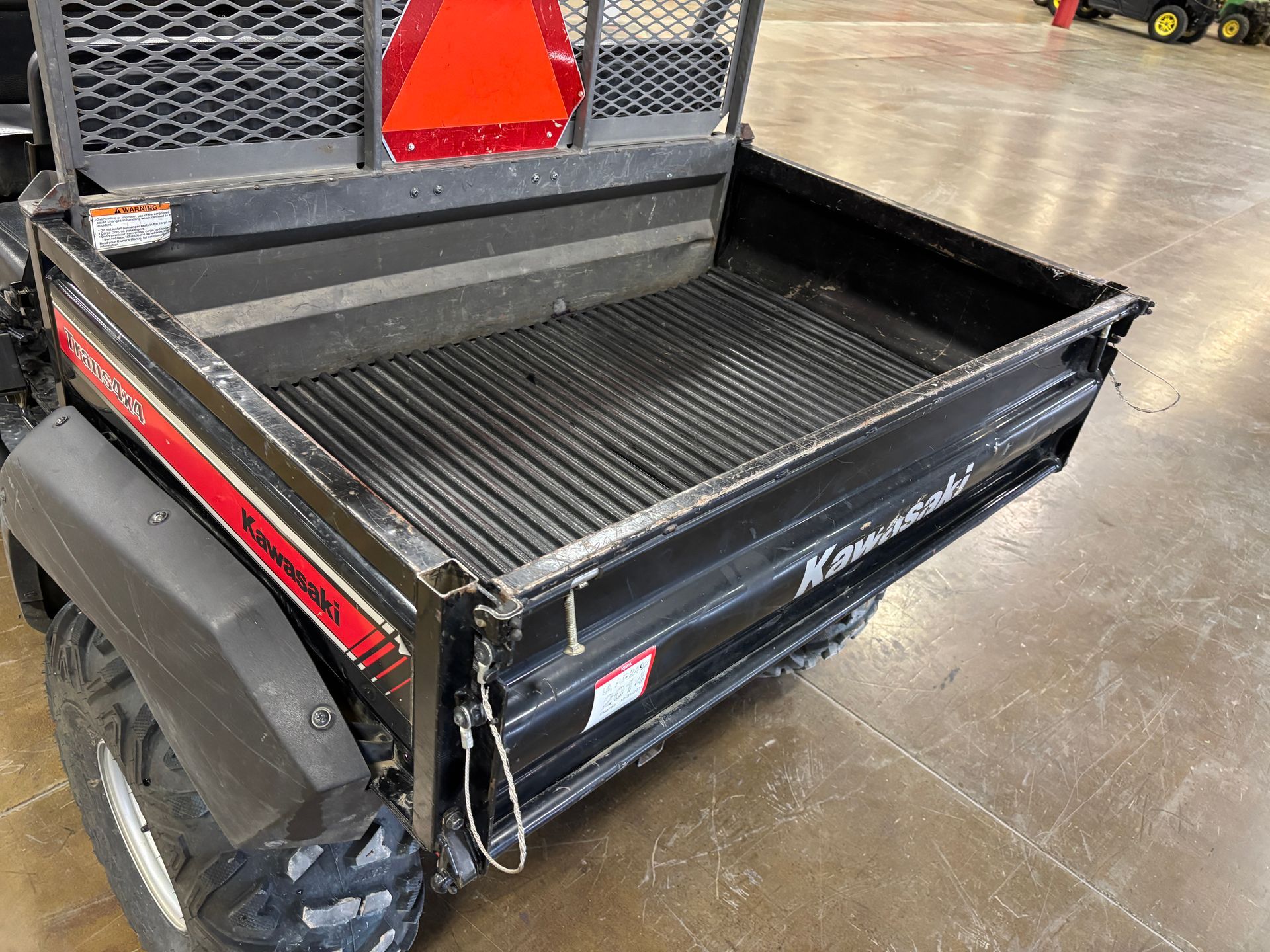 Black Kawasaki Mule utility vehicle bed with red reflective triangle, side view.