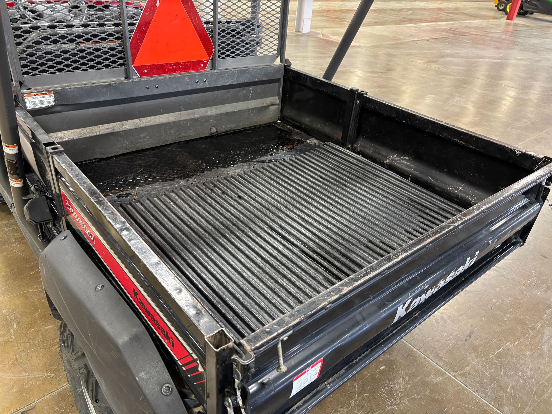 Black utility vehicle bed with ribbed floor, red triangle, Kawasaki logo.