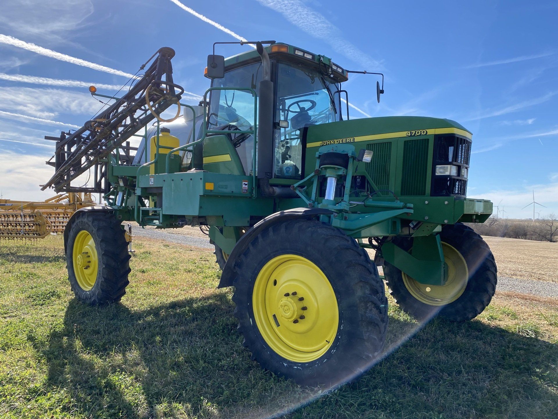 Green John Deere sprayer on a grassy field, with yellow wheels and a raised boom.