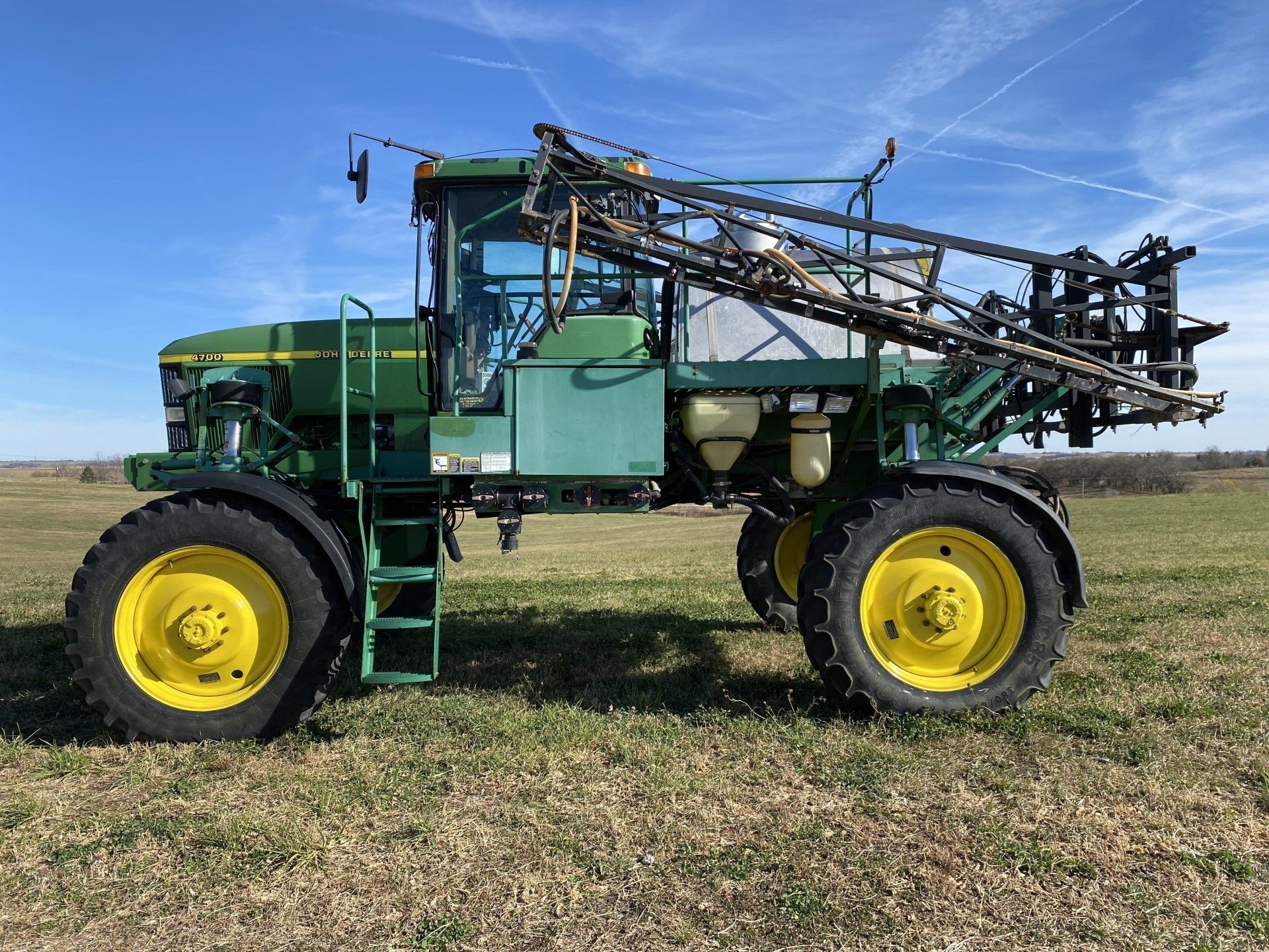 Green and yellow John Deere agricultural sprayer on a grassy field under a blue sky.