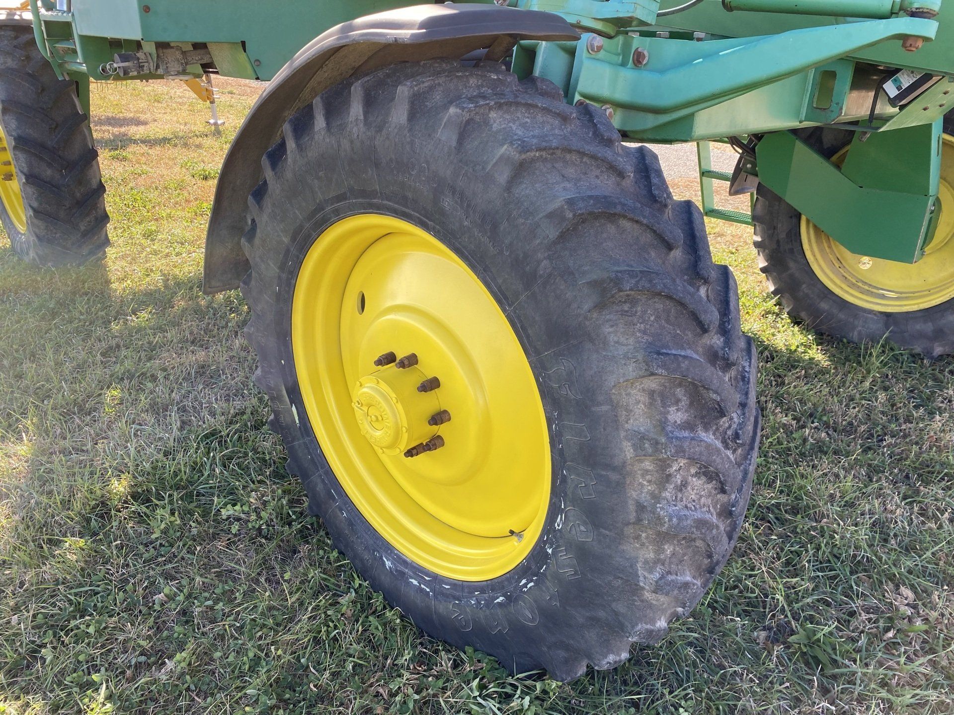 Close-up of a John Deere tractor wheel. Yellow wheel and tire in a grassy field.