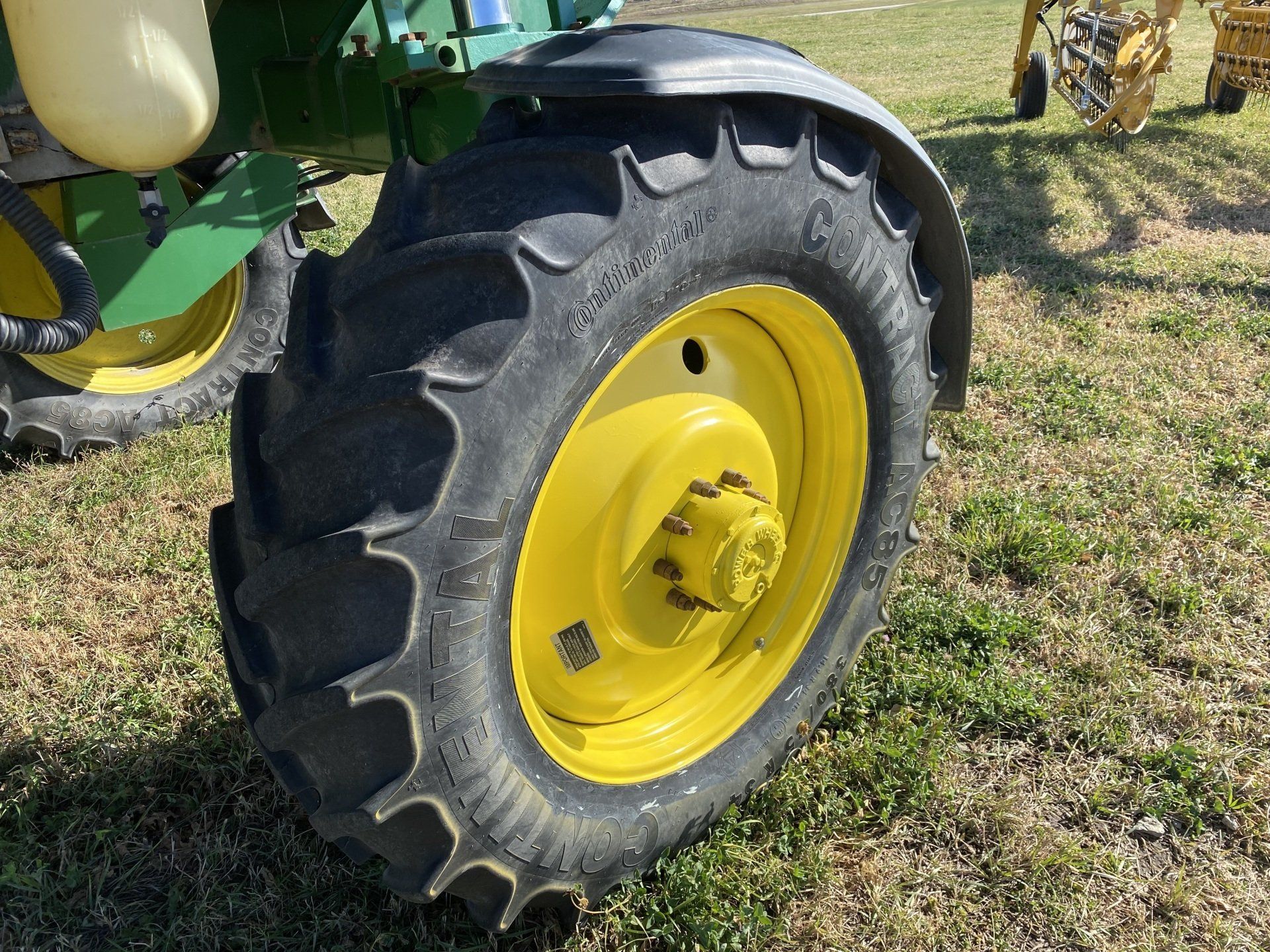 Yellow tractor wheel with black tire and fender in grassy field.