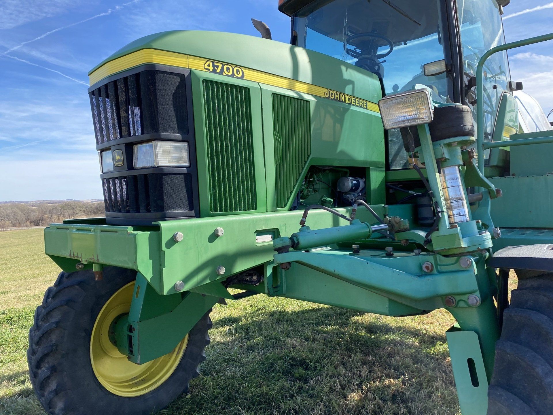 Green John Deere 6750 forage harvester in a field, with a black grill and yellow wheels.