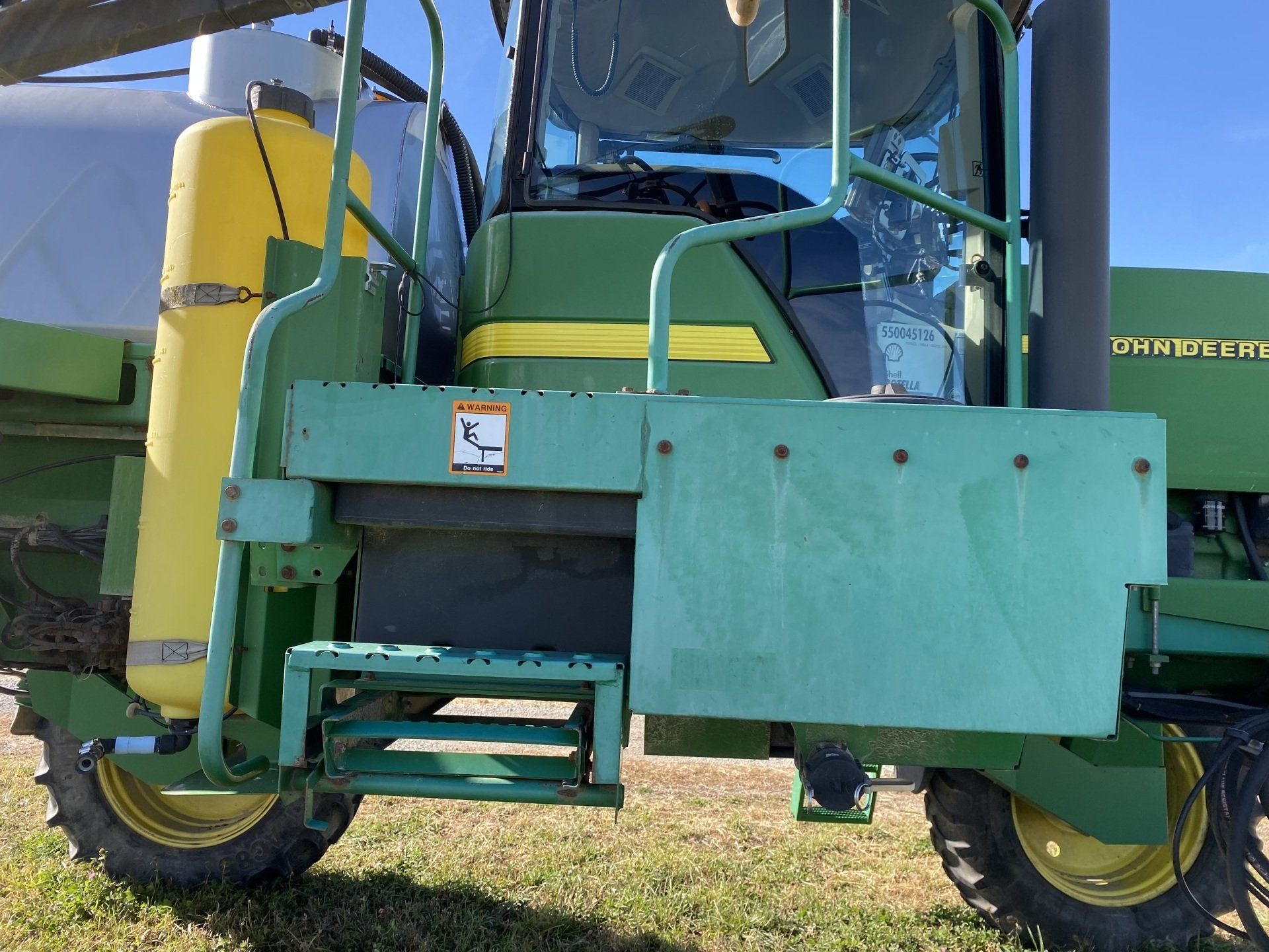 Green John Deere agricultural sprayer, steps, yellow wheels, tank.