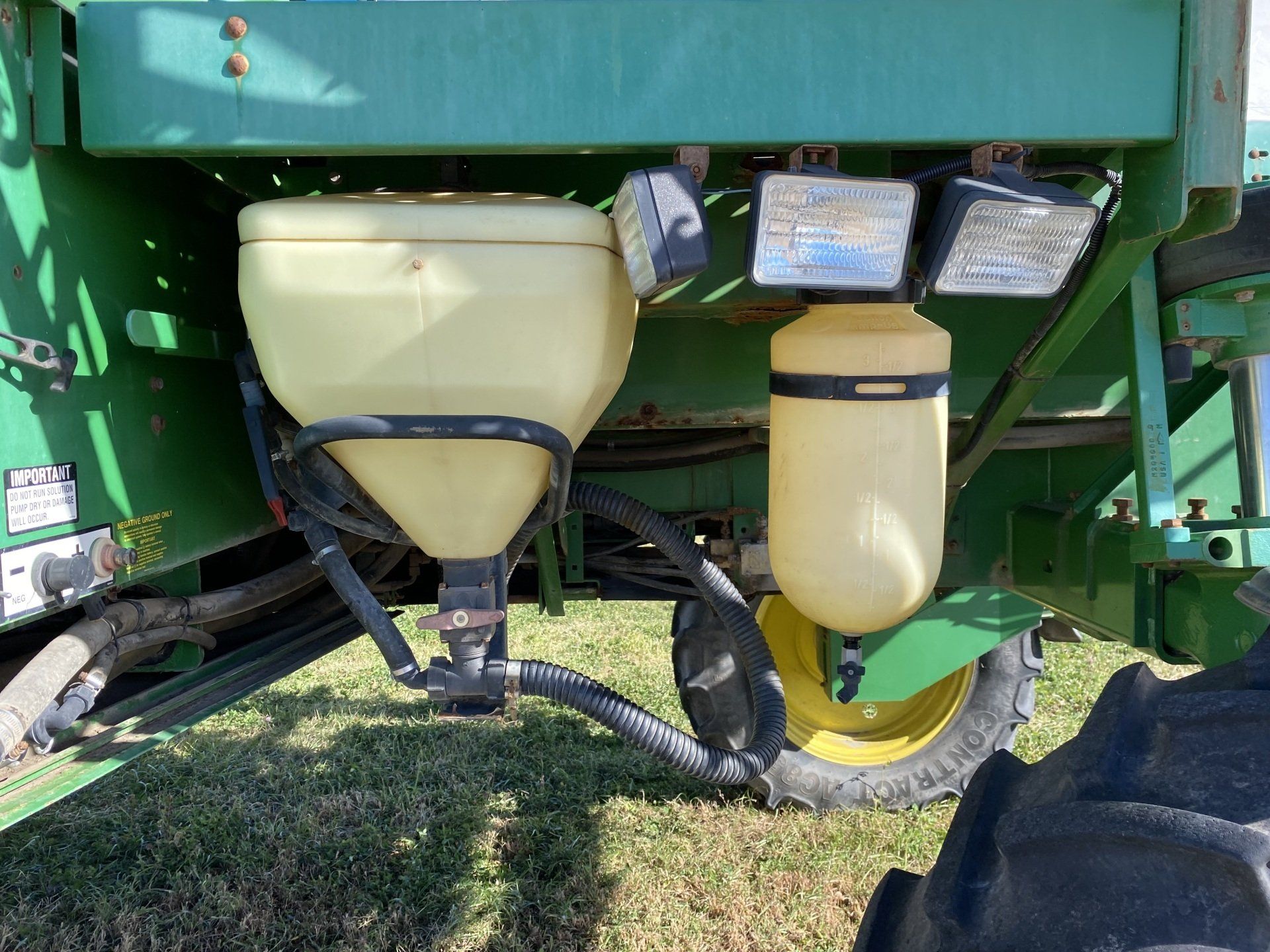 Green agricultural planter with yellow tanks and a black hose, near a tractor tire.