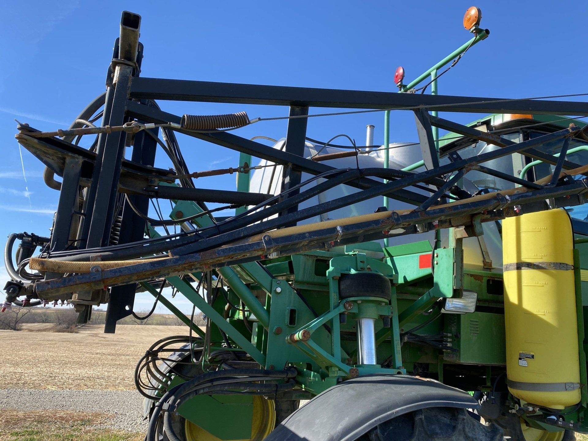 Close-up of a green and black John Deere agricultural sprayer with a blue sky background.