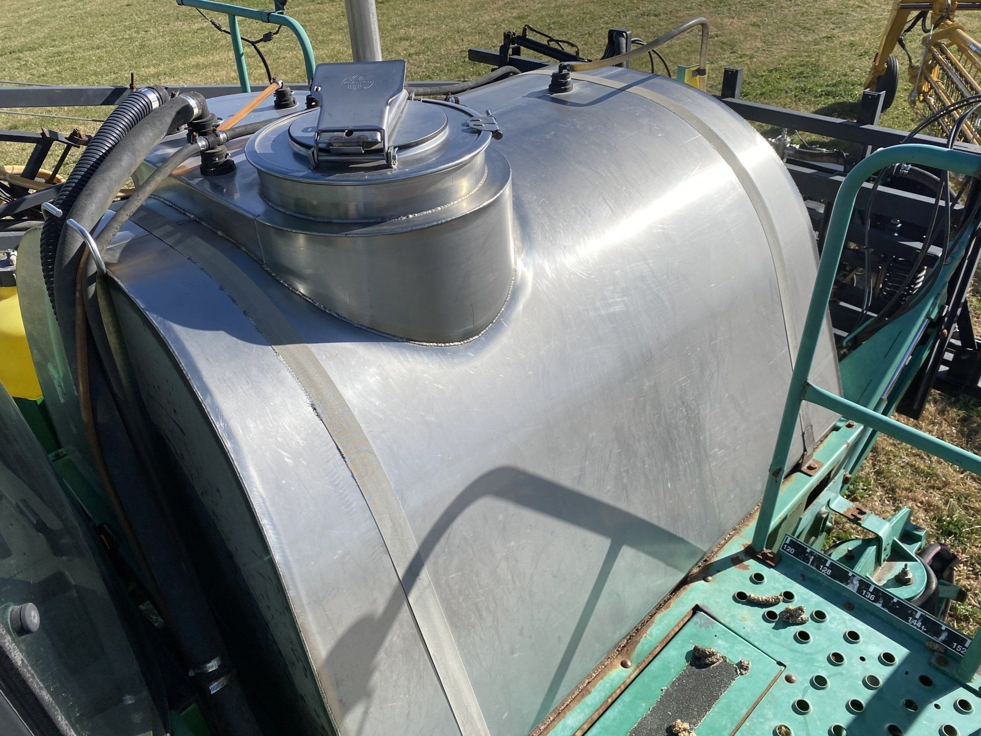 Green John Deere agricultural sprayer against a clear blue sky.