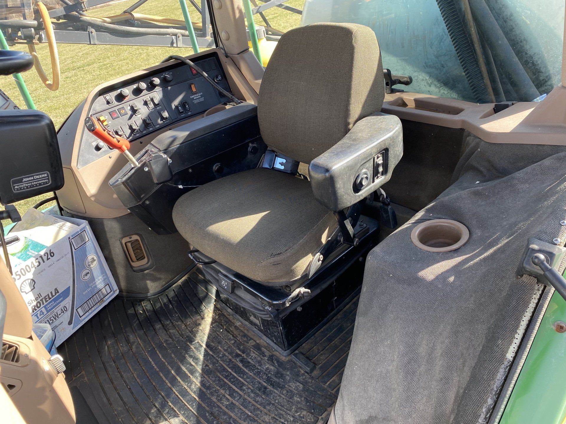 Interior of a John Deere tractor cab with a seat, control panel, and cup holder.