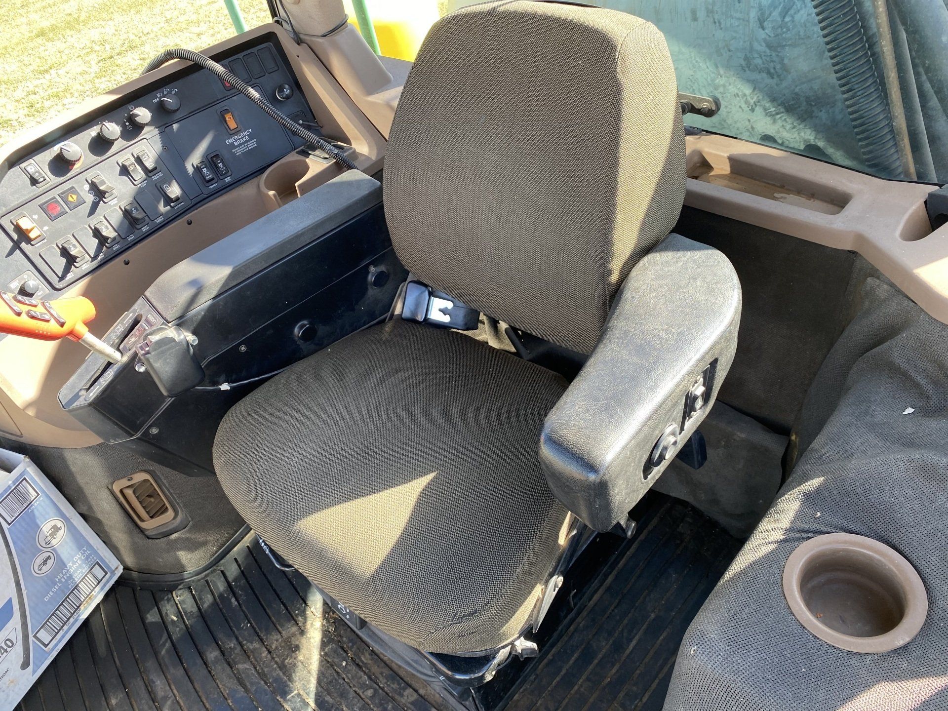 Interior view of a tractor cab: seat, armrest, controls, and cup holder.
