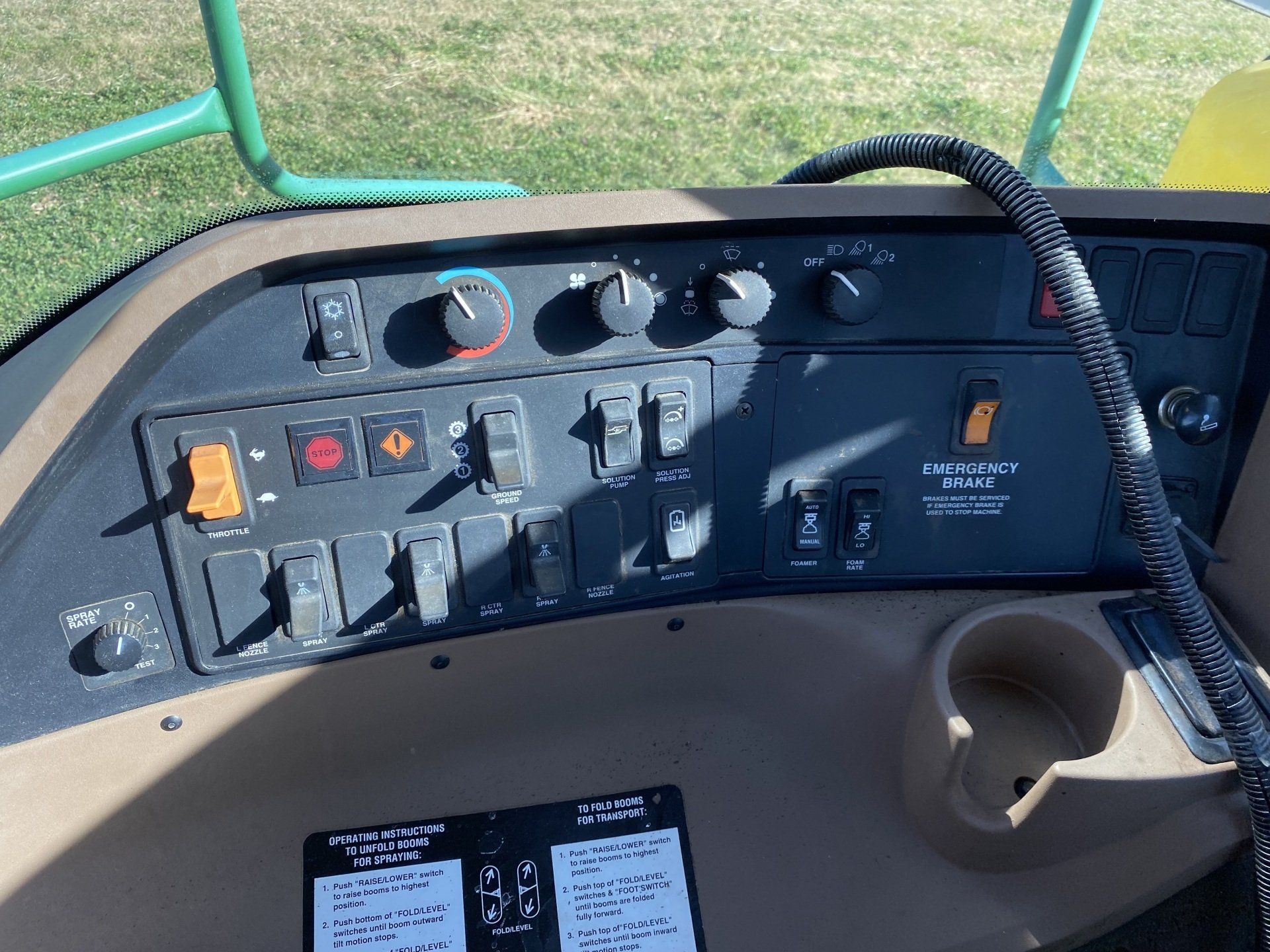 Dashboard of a John Deere farm machine, featuring switches, knobs, and a cup holder.