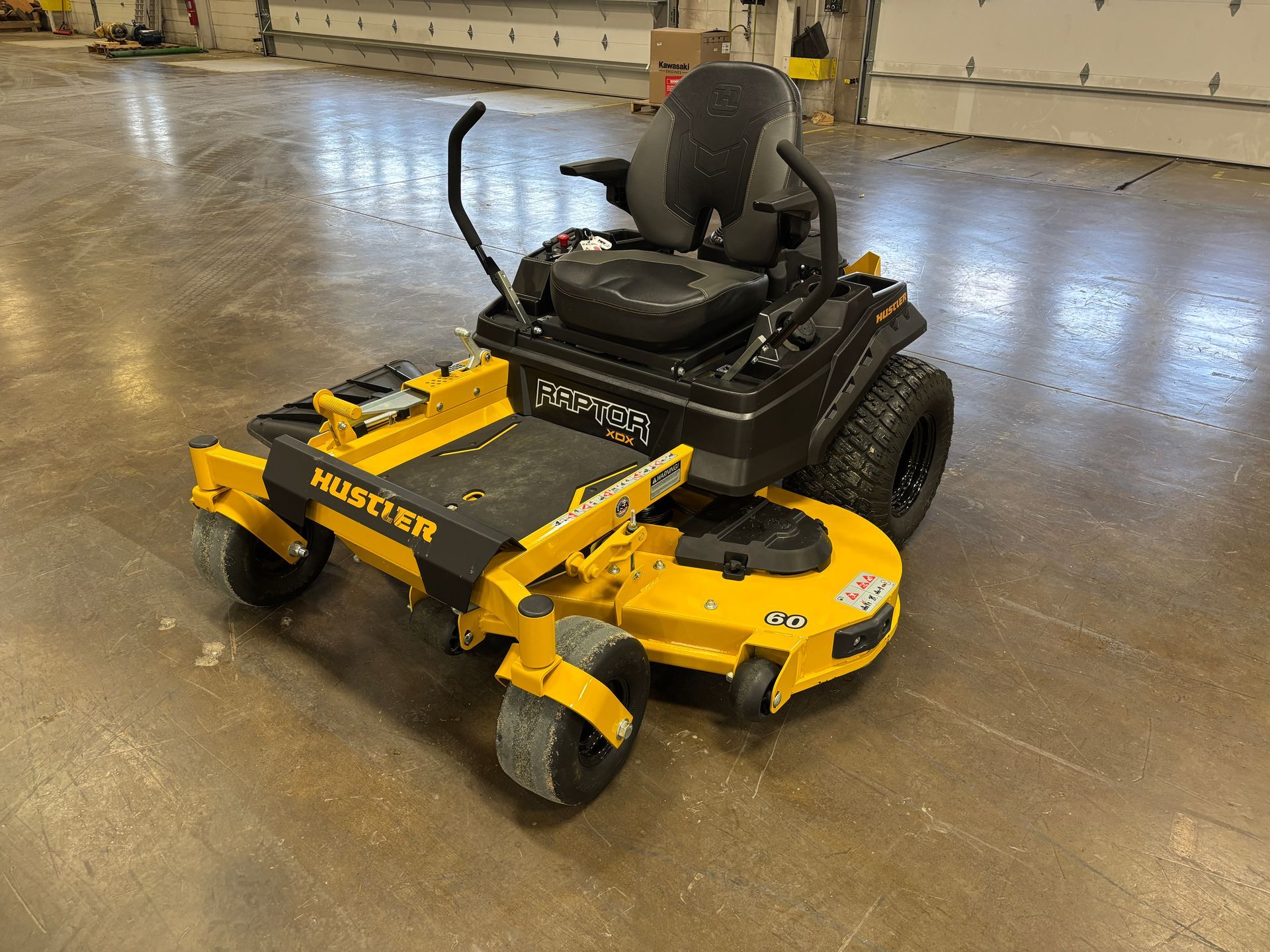 Yellow and black Hustler zero-turn lawn mower on a concrete floor.