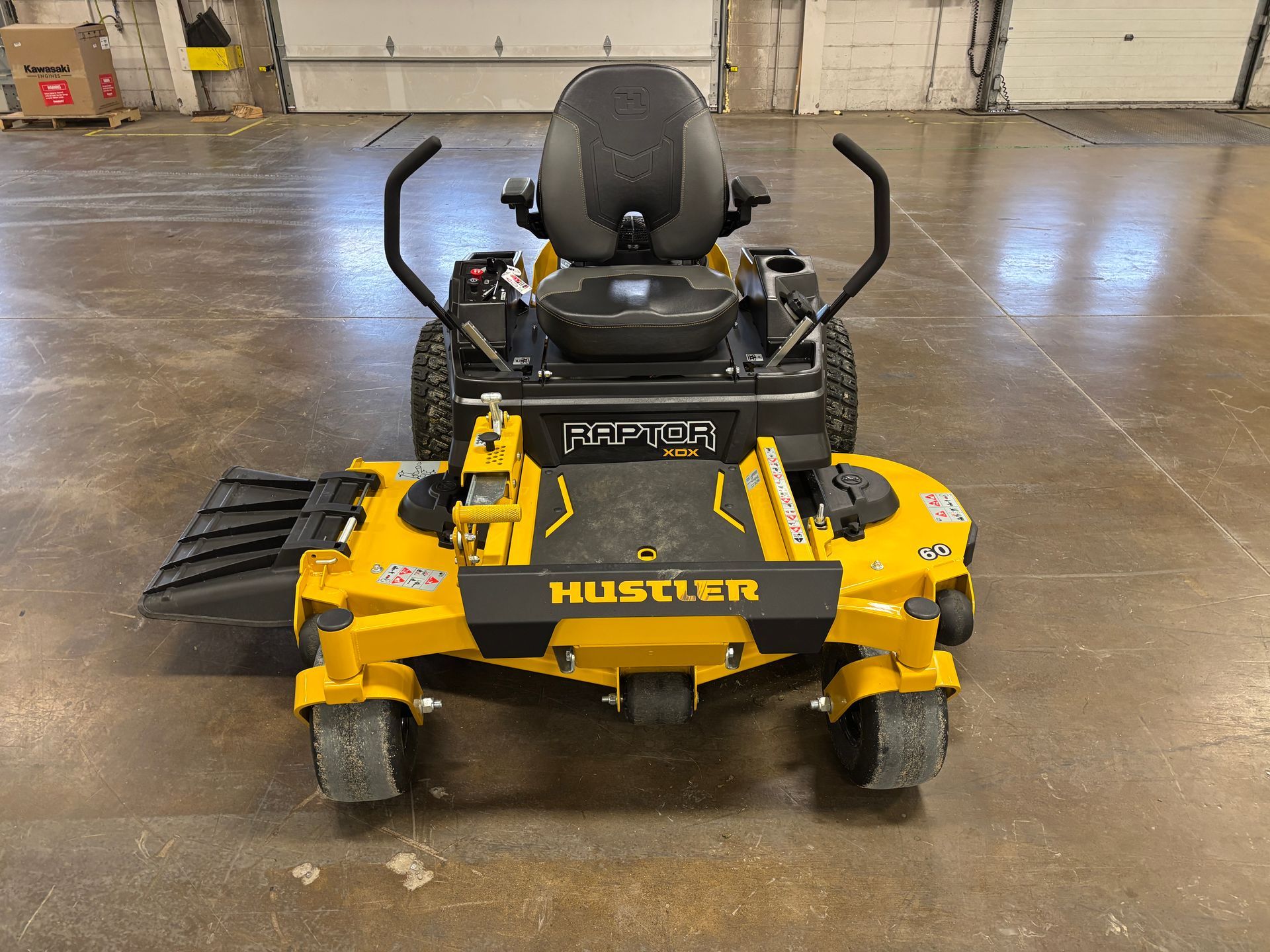 Yellow Hustler zero-turn lawnmower on a gray concrete floor, viewed from the front.