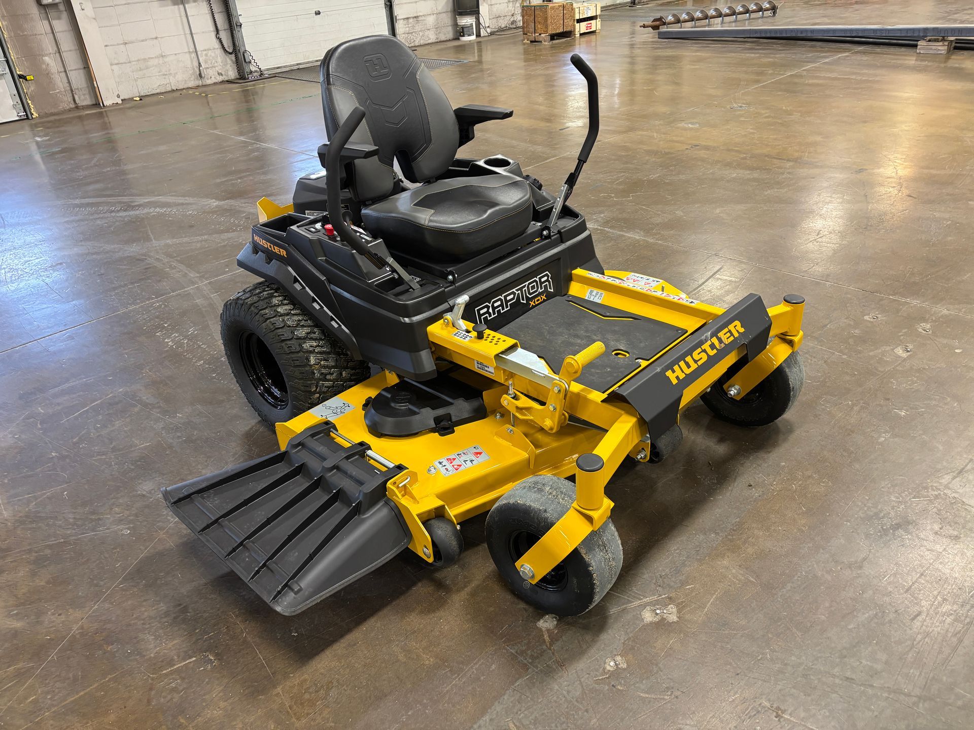 Yellow and black Hustler zero-turn mower on a concrete floor, angled view.