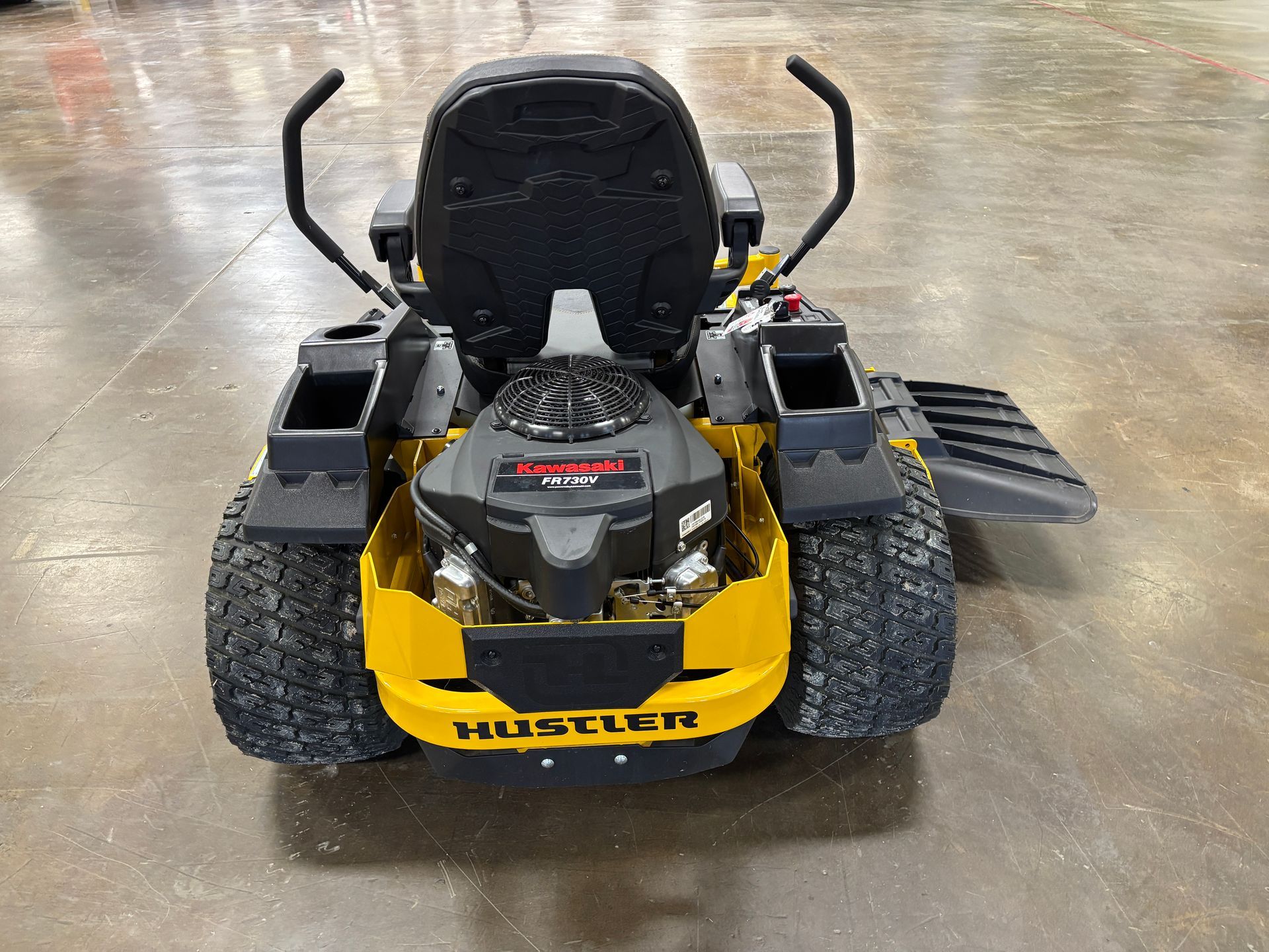 Yellow and black Hustler zero-turn lawn mower, frontal view on a concrete floor.