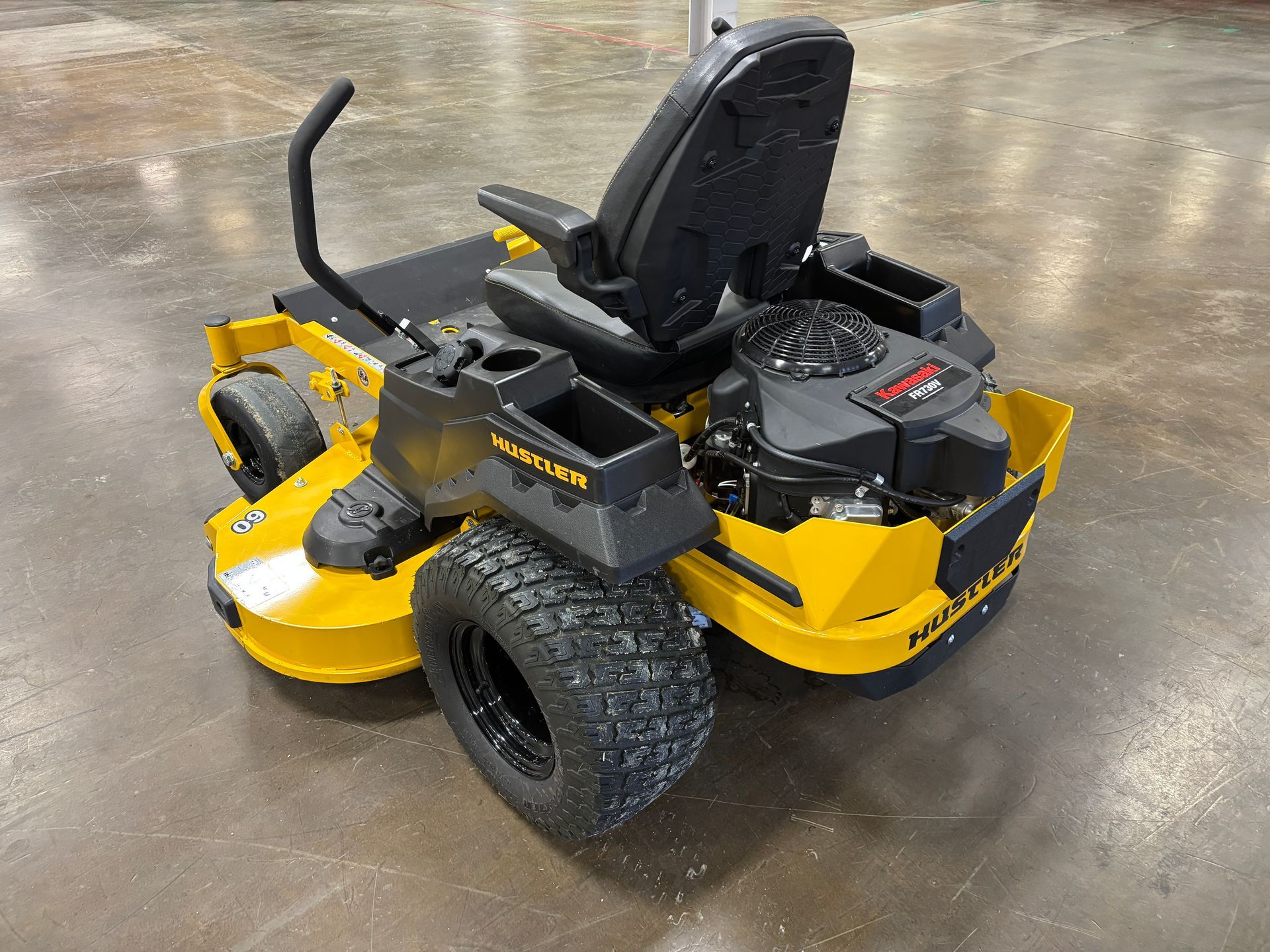 Yellow and black Hustler zero-turn lawnmower on a concrete floor.