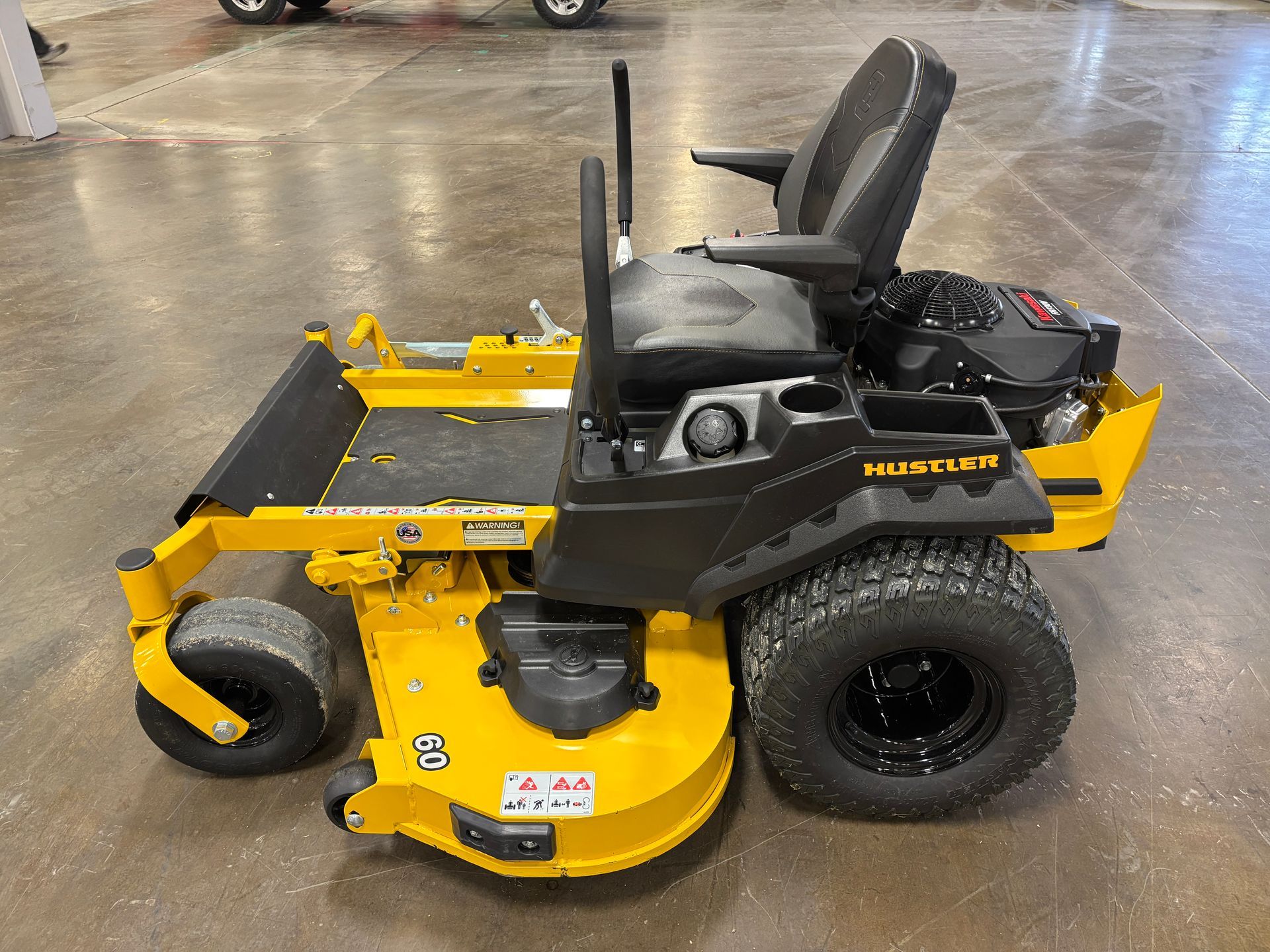 Yellow and black Hustler zero-turn lawn mower on a concrete floor.