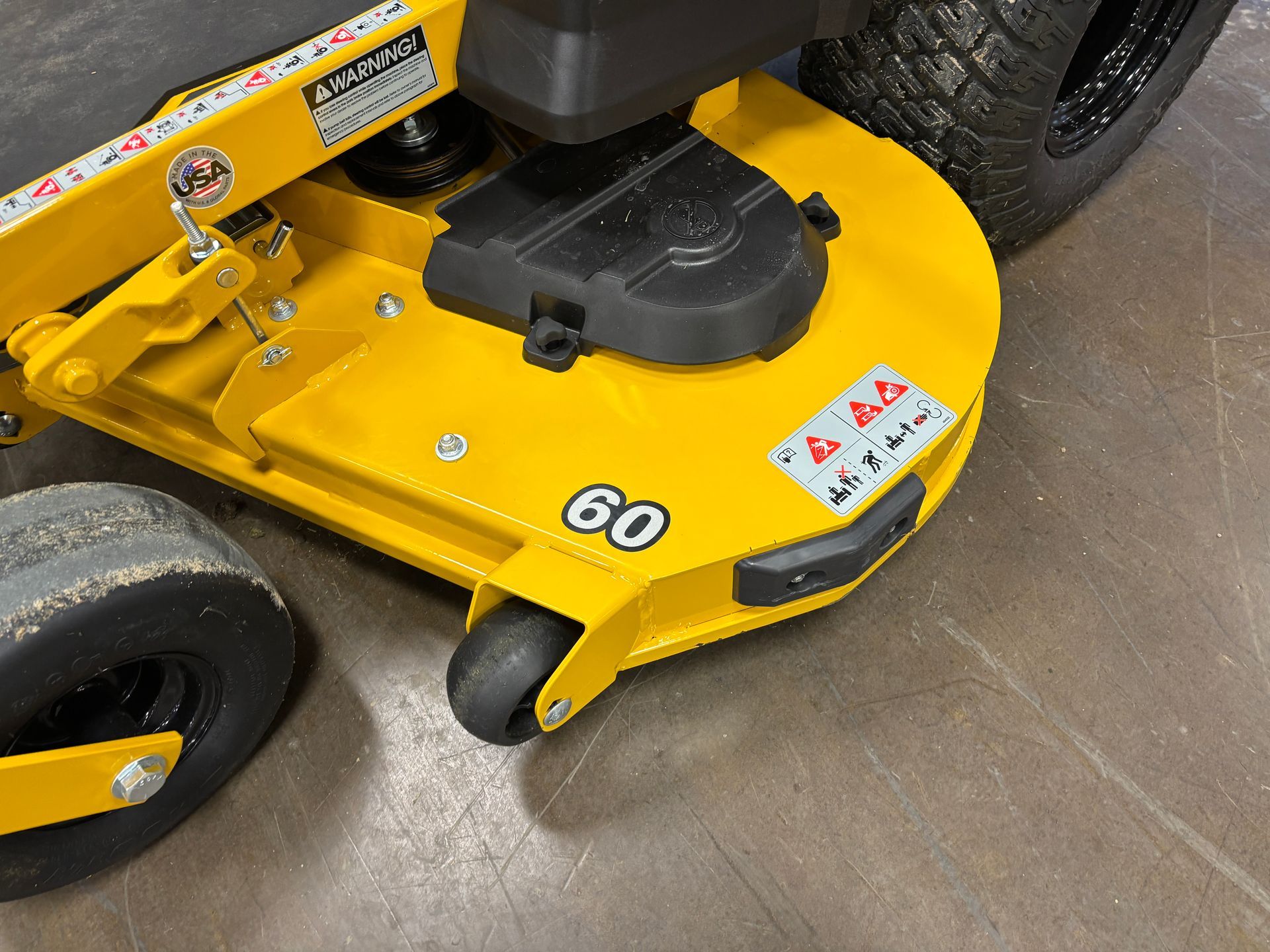 Yellow lawn mower deck with a 60 label and black tires.