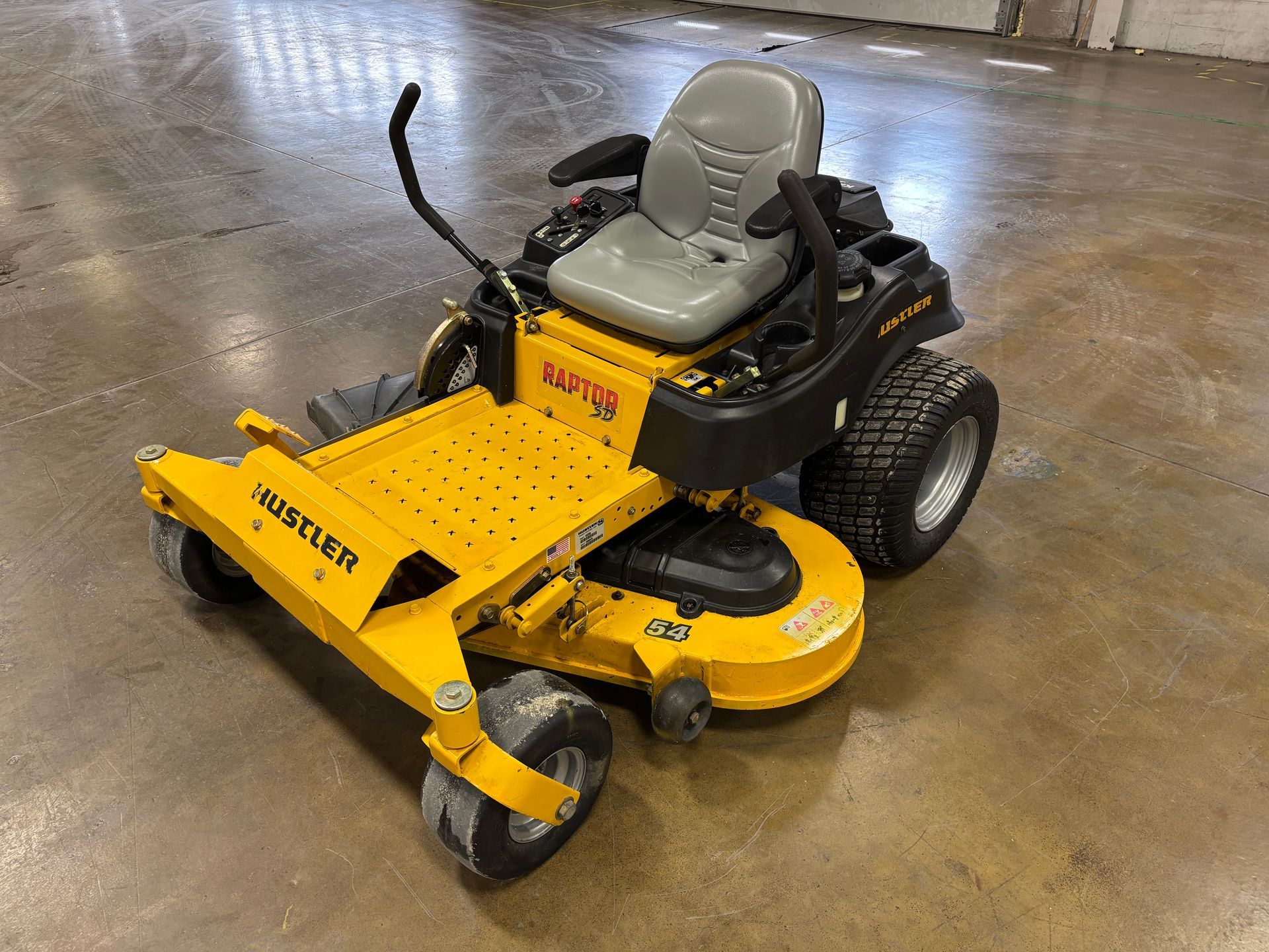 Yellow and black Hustler zero-turn lawn mower on a concrete floor.
