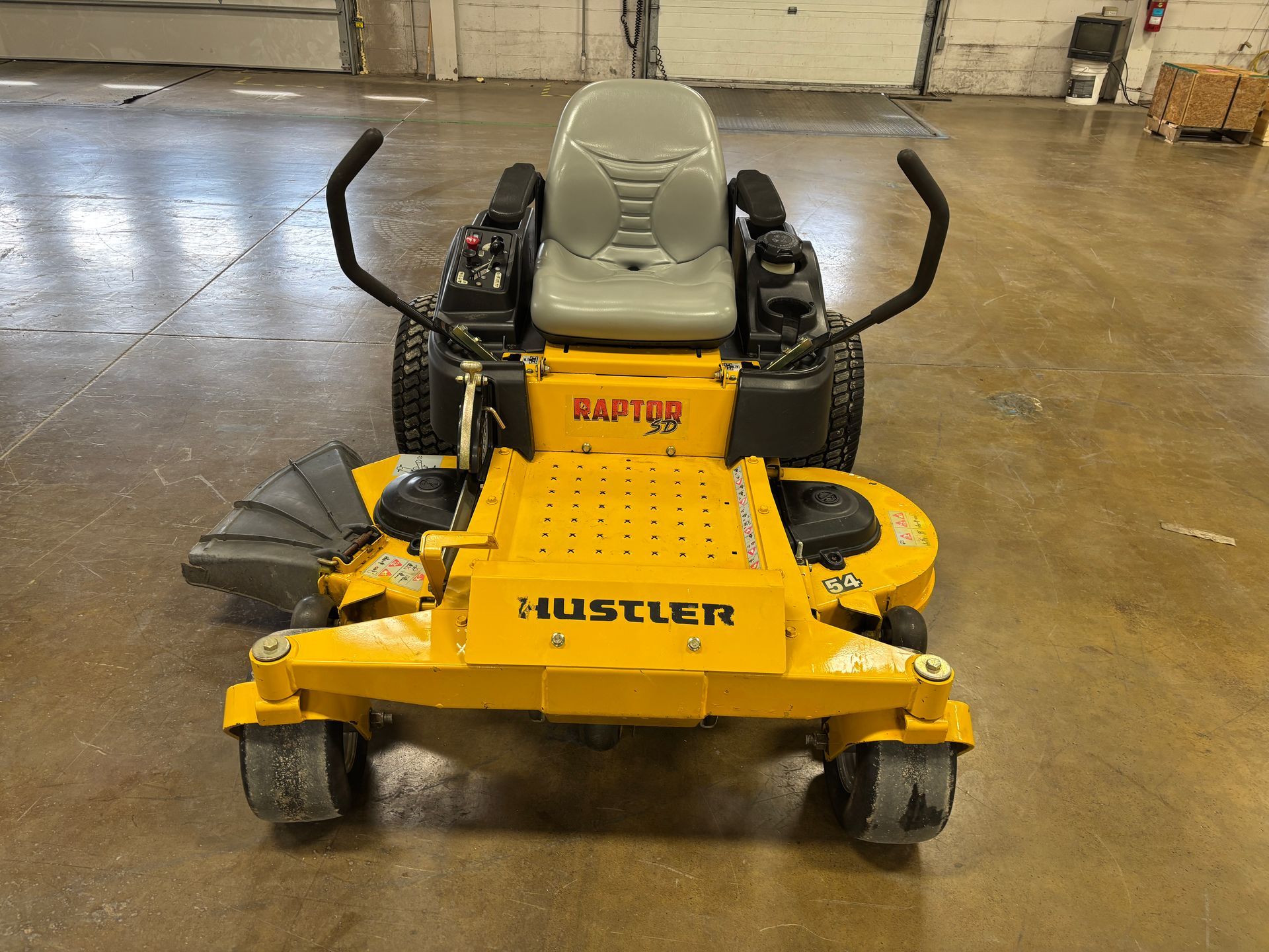 Yellow Hustler Raptor zero-turn lawn mower on a concrete floor.