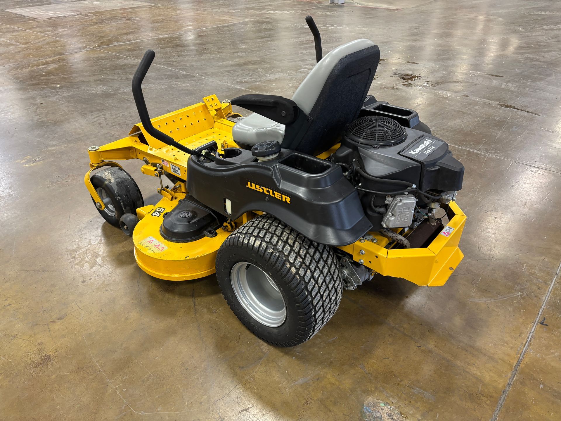Yellow and black lawnmower on a concrete surface. Features large rear tires, a seat, and a motor.