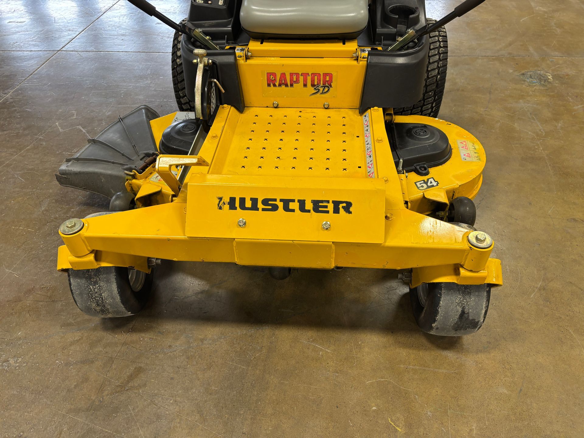 Yellow Hustler Raptor XP zero-turn lawn mower on a concrete floor.
