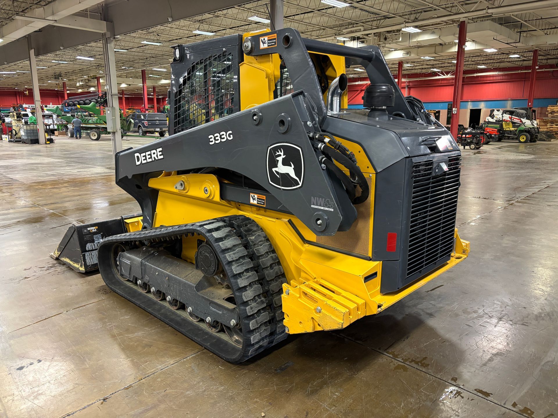 Yellow and black John Deere compact track loader with a front bucket on a gray concrete floor, back angled shot.