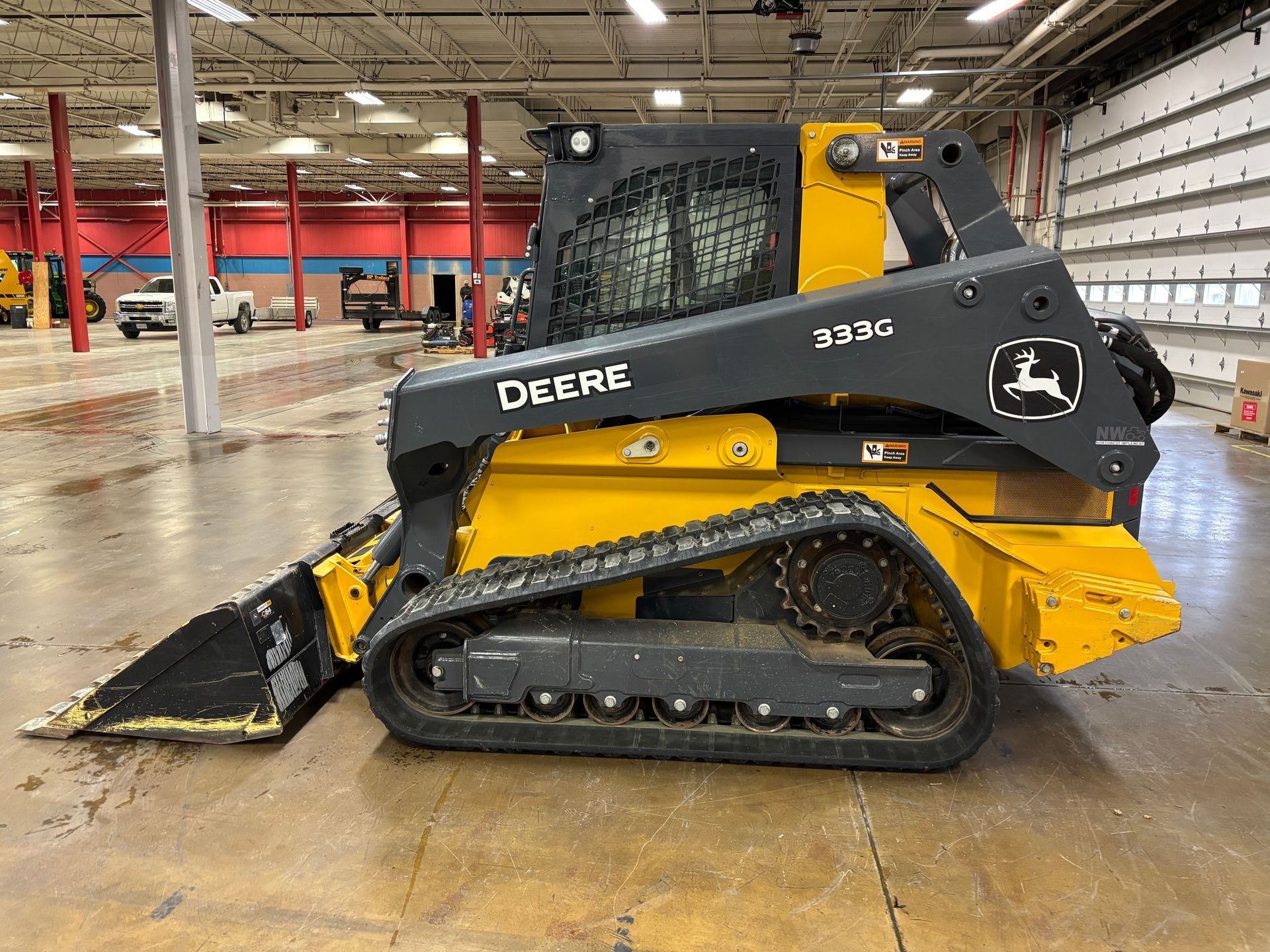 Yellow and black John Deere compact track loader with a front bucket on a gray concrete floor, side view shot.