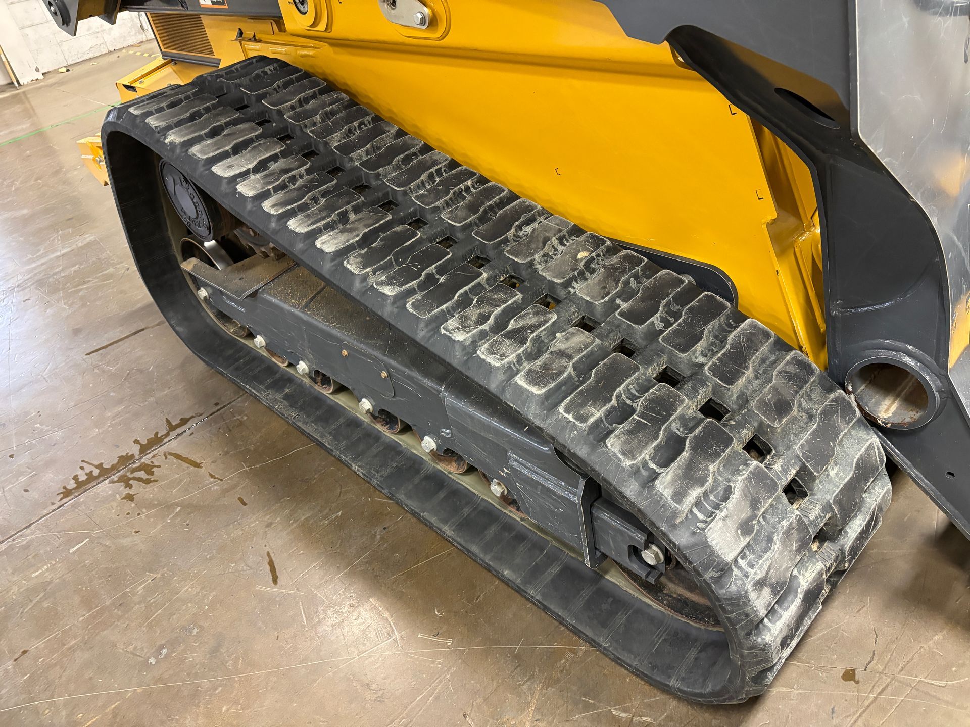 Yellow and black track of a skid steer loader on a concrete floor.