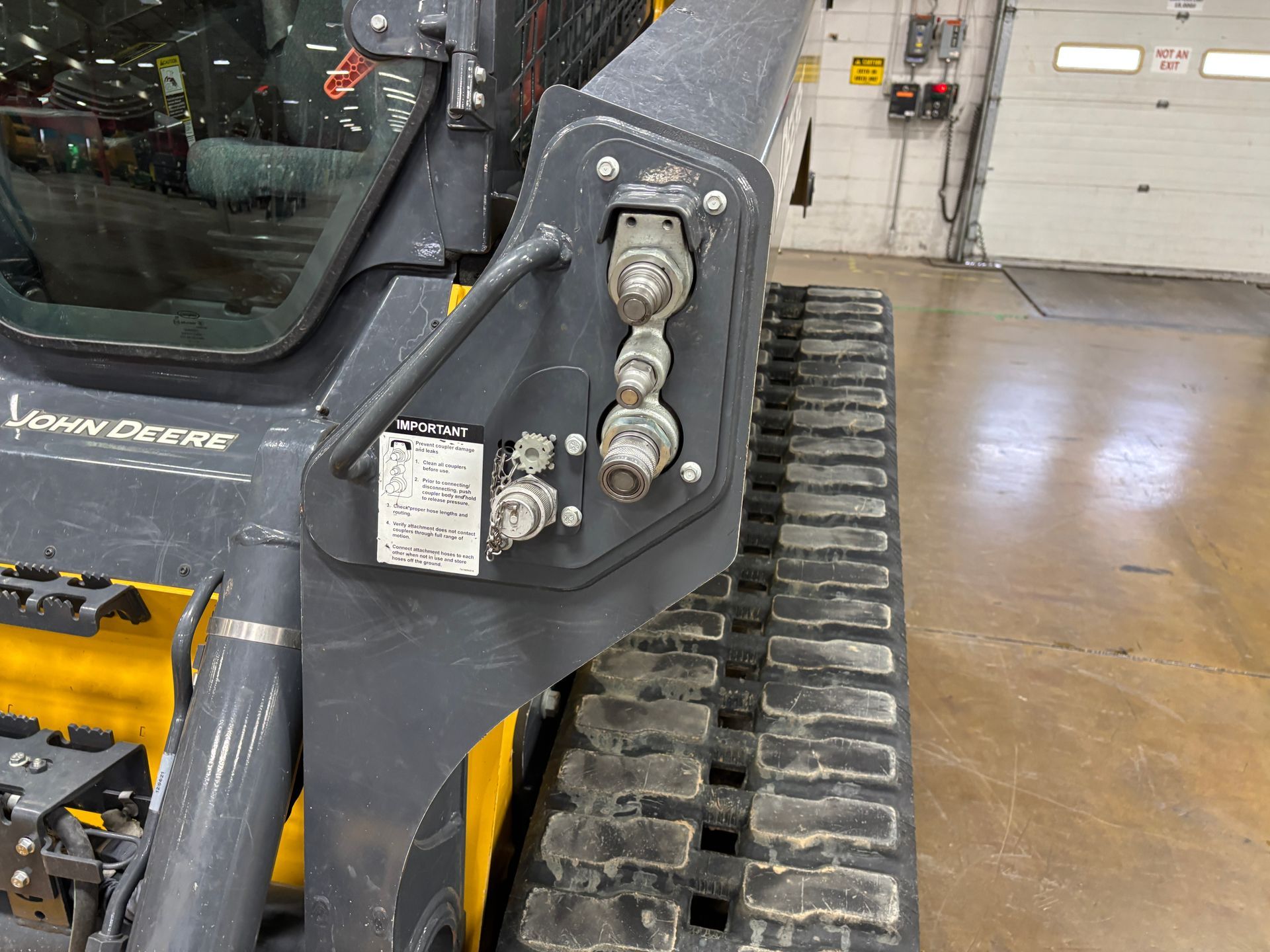 Close-up of a John Deere compact track loader, showing hydraulic fittings.