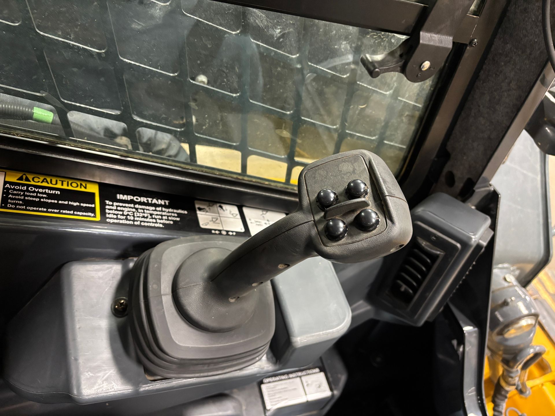 Close-up of a compact track loader joystick with buttons, inside the cab.
