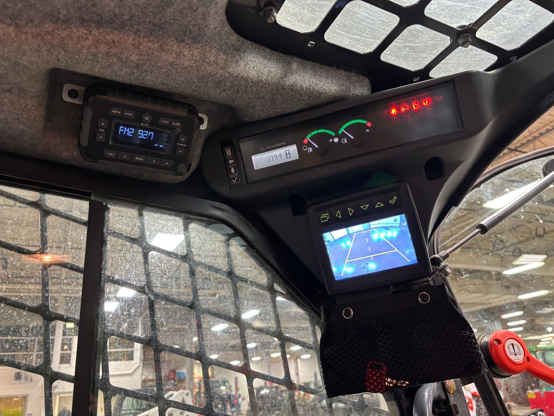 Interior view of a compact track loader cab, showing radio, gauges, and a backup camera screen.