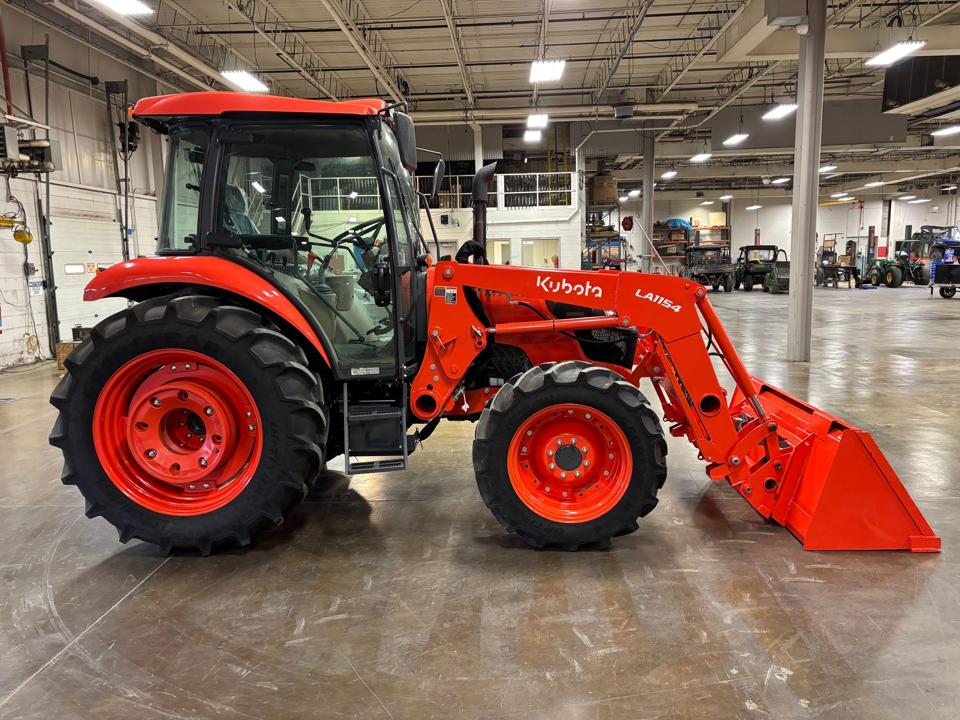 Orange tractor with loader bucket in a large industrial building.