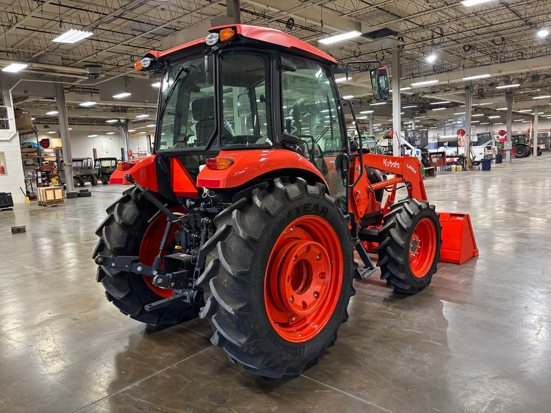 Orange tractor with a cab, black tires, and front loader in a large warehouse.
