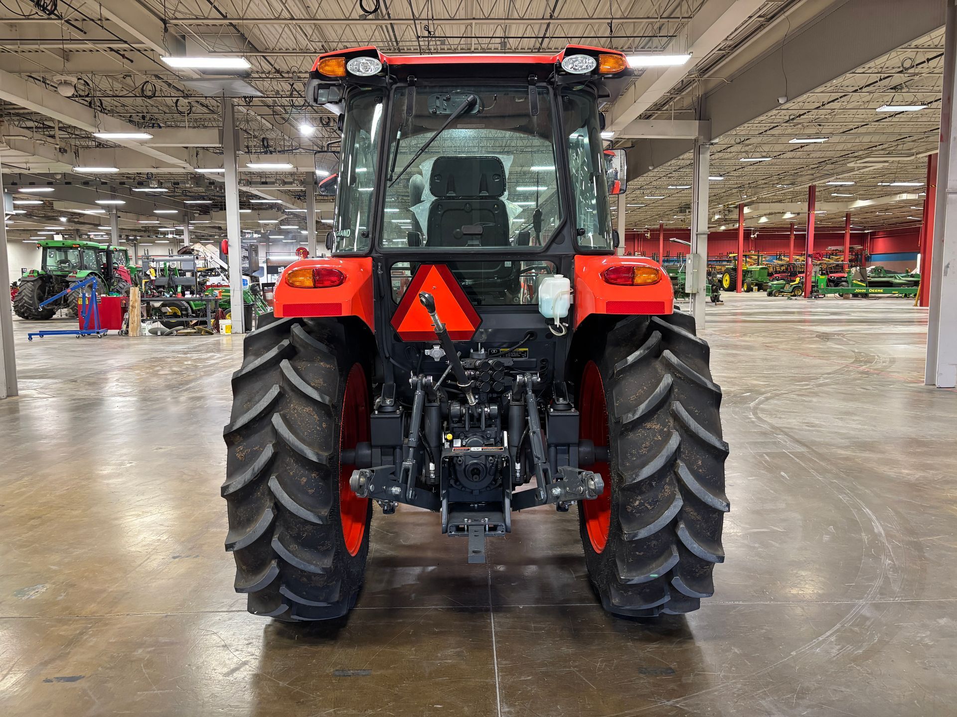 Orange tractor, rear view, inside a building. Large tires and lights are visible.