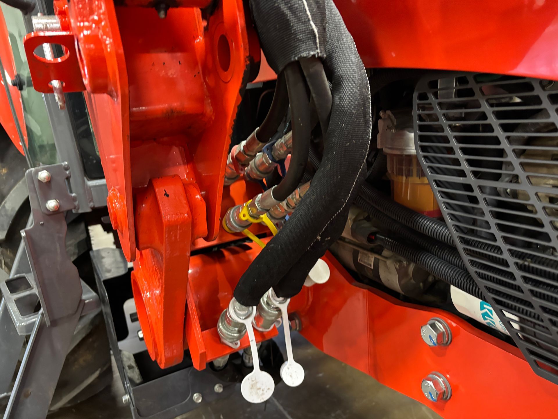 Close-up of orange tractor hydraulics with multiple black hoses and silver connectors, secured with white tags.
