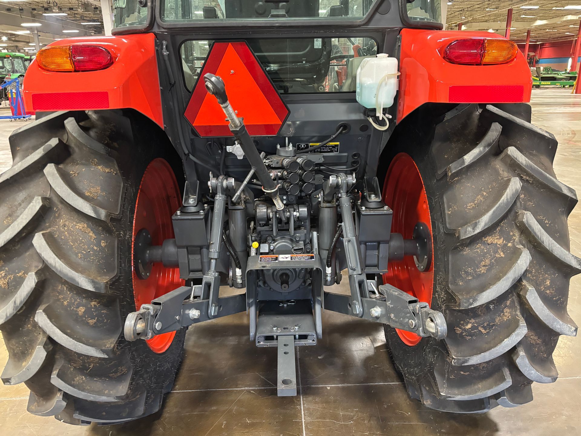 Rear view of a red tractor with large, black tires and orange wheels. A black hitch and warning triangle are visible.