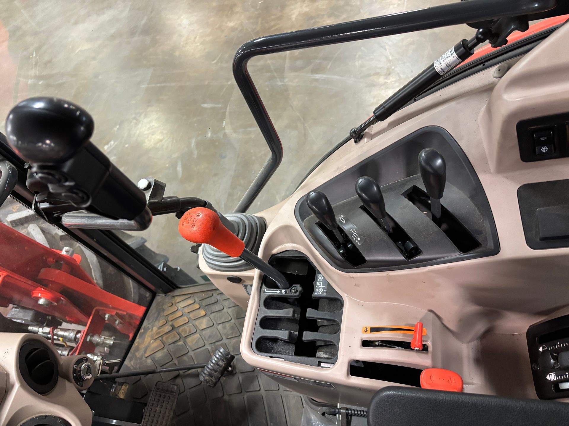 Interior view of a tractor cockpit with levers, gear shift, and controls in a tan-colored setting.