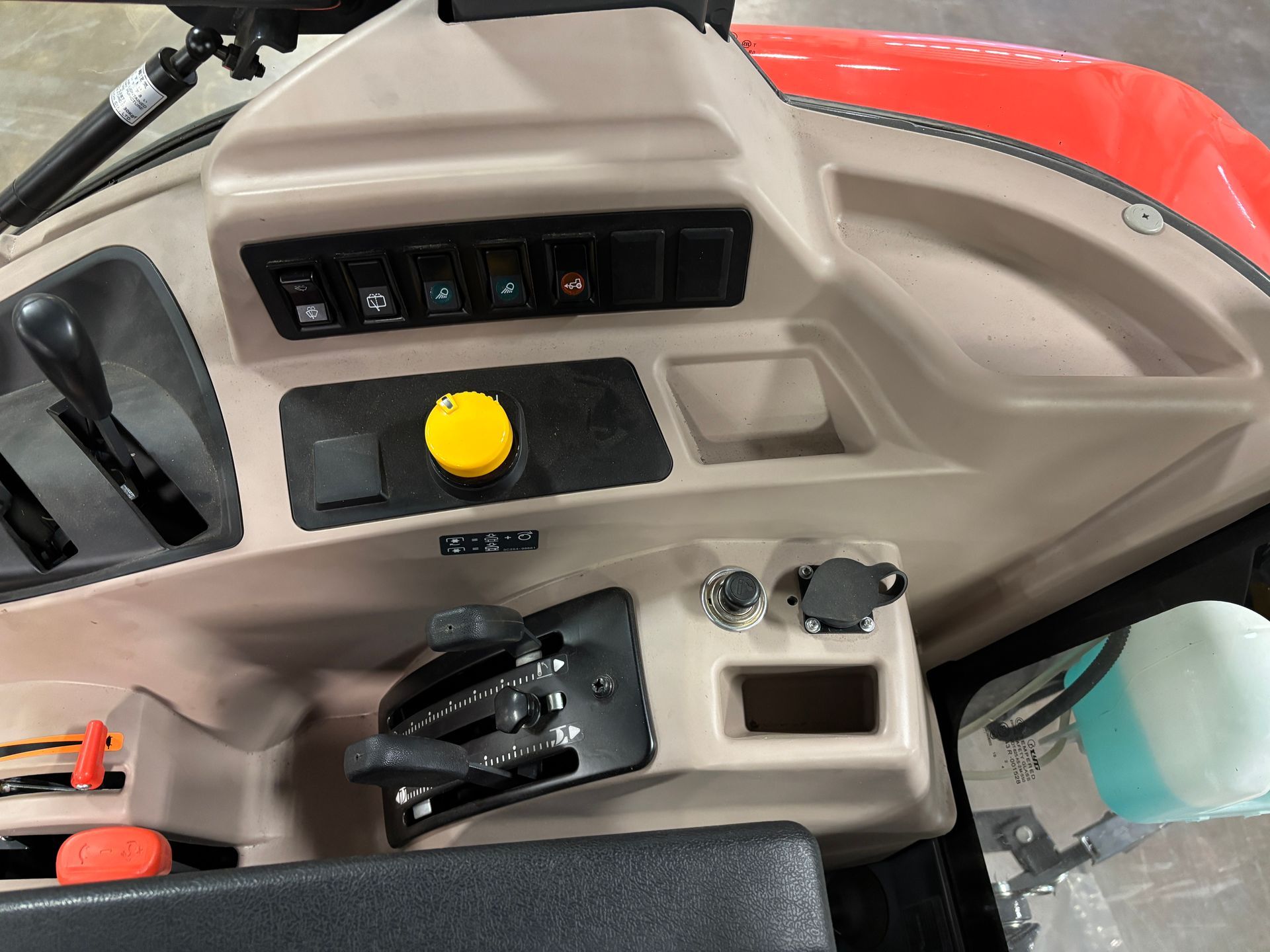 Dashboard of a red tractor with switches, a large yellow button, and gear levers.