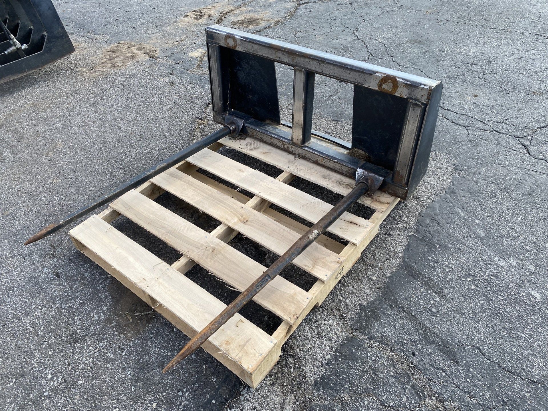 Forklift forks attached to a wooden pallet on asphalt.